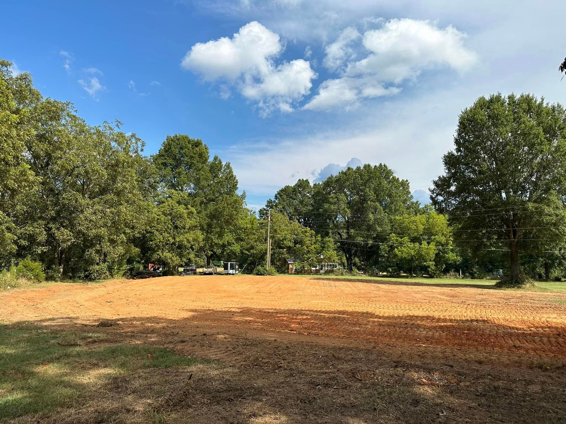 A large dirt field with trees in the background and a blue sky with clouds.