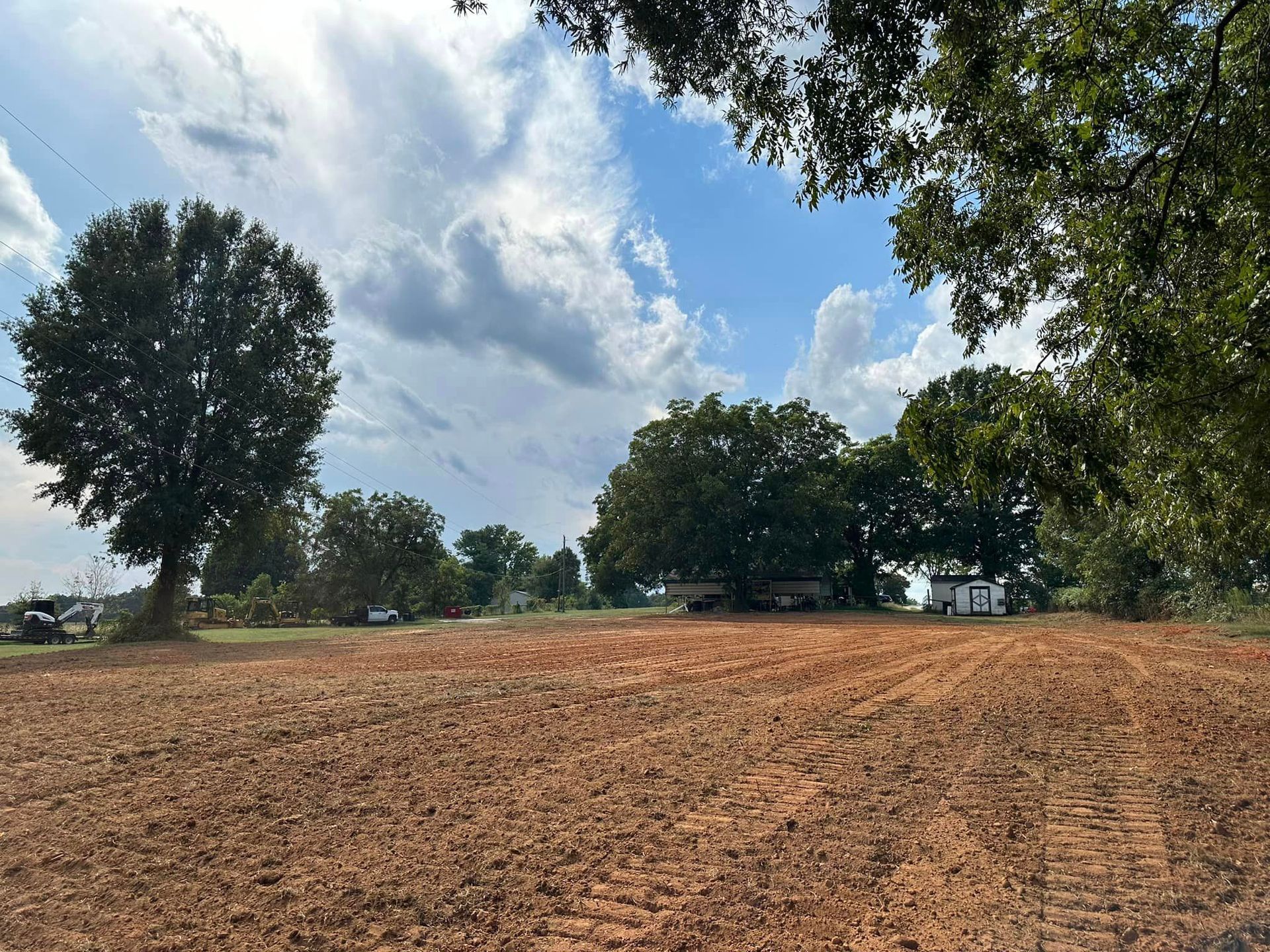 A large dirt field with trees in the background and a blue sky with clouds.