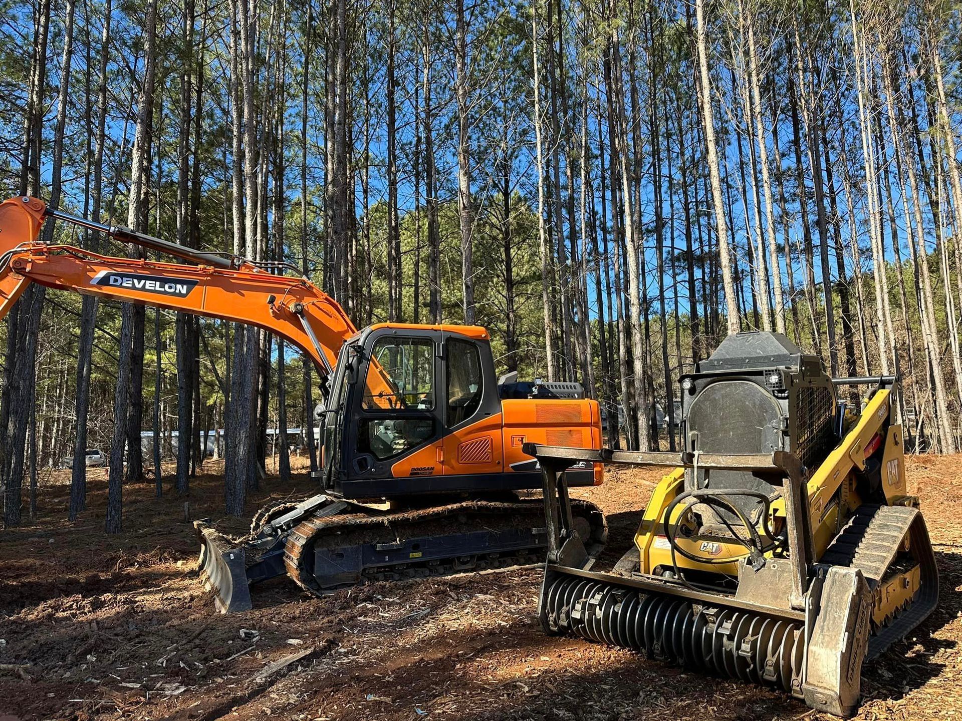 A bulldozer and an excavator are sitting in the middle of a forest.