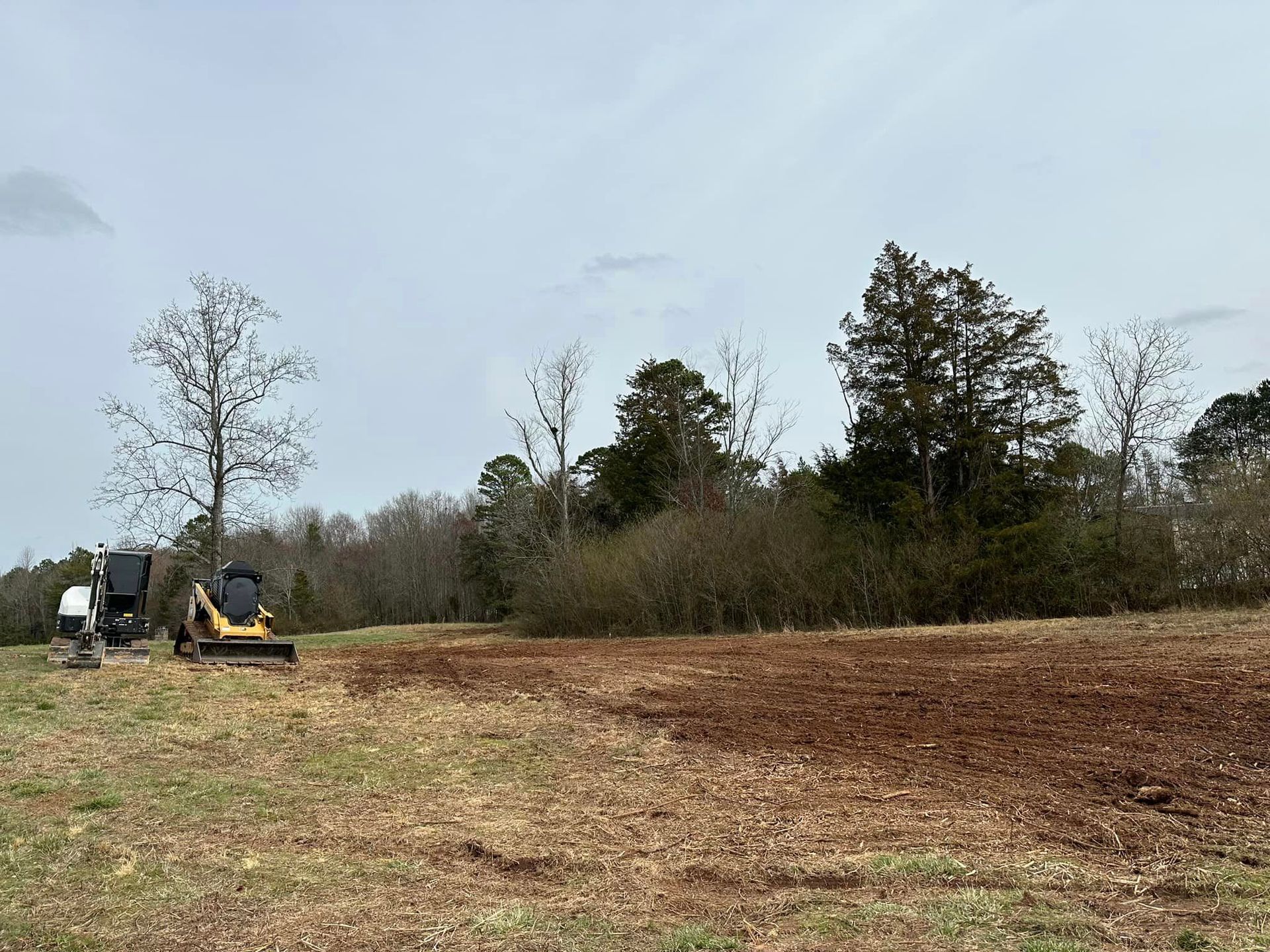 A bulldozer is plowing a field with trees in the background.
