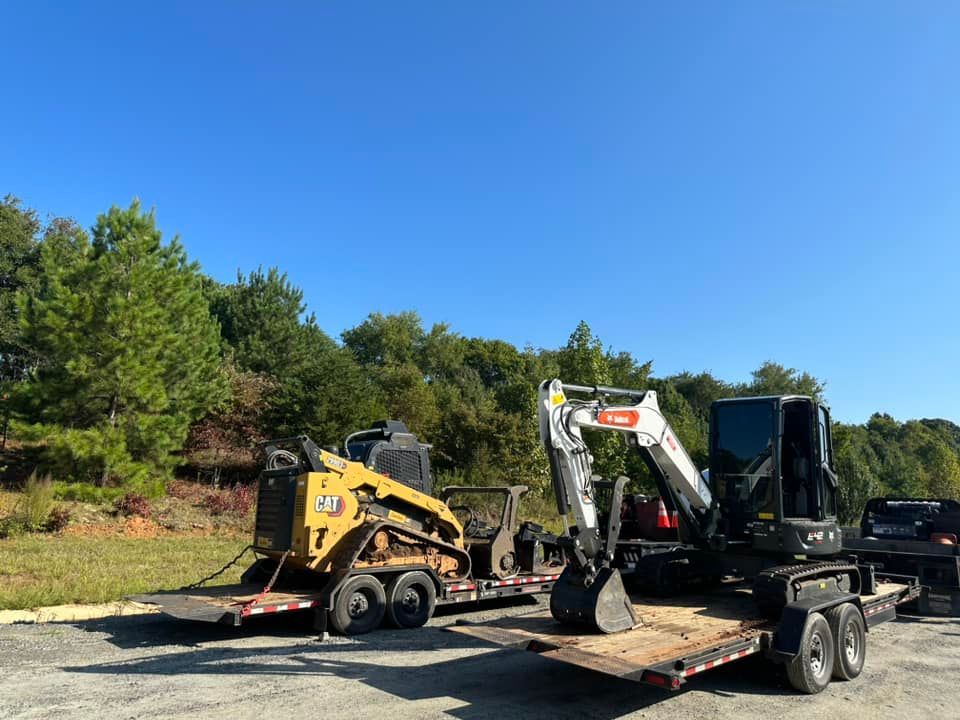 A bulldozer and an excavator are on a trailer in a parking lot.