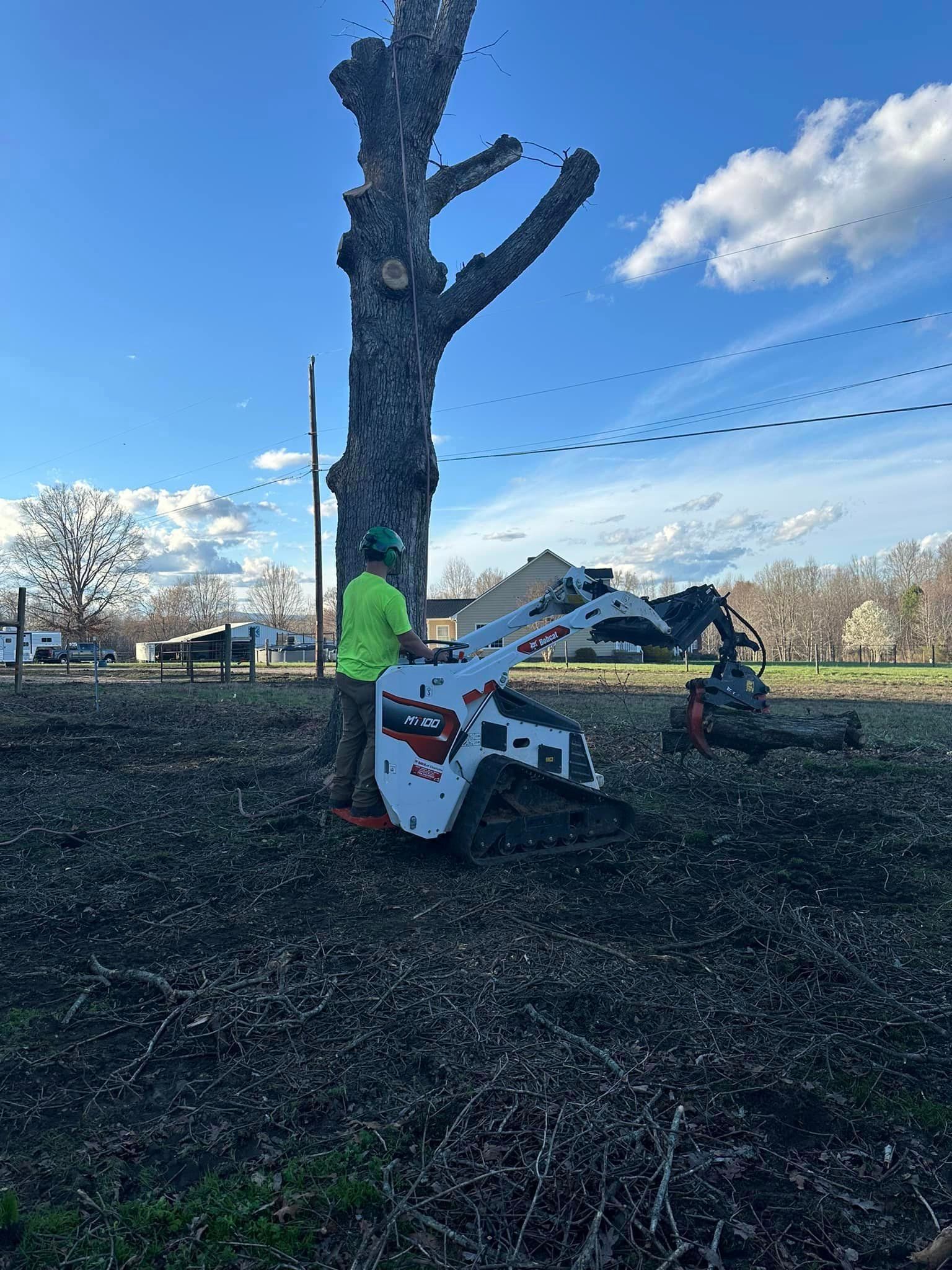 A man is standing next to a bobcat stump grinder in a field.