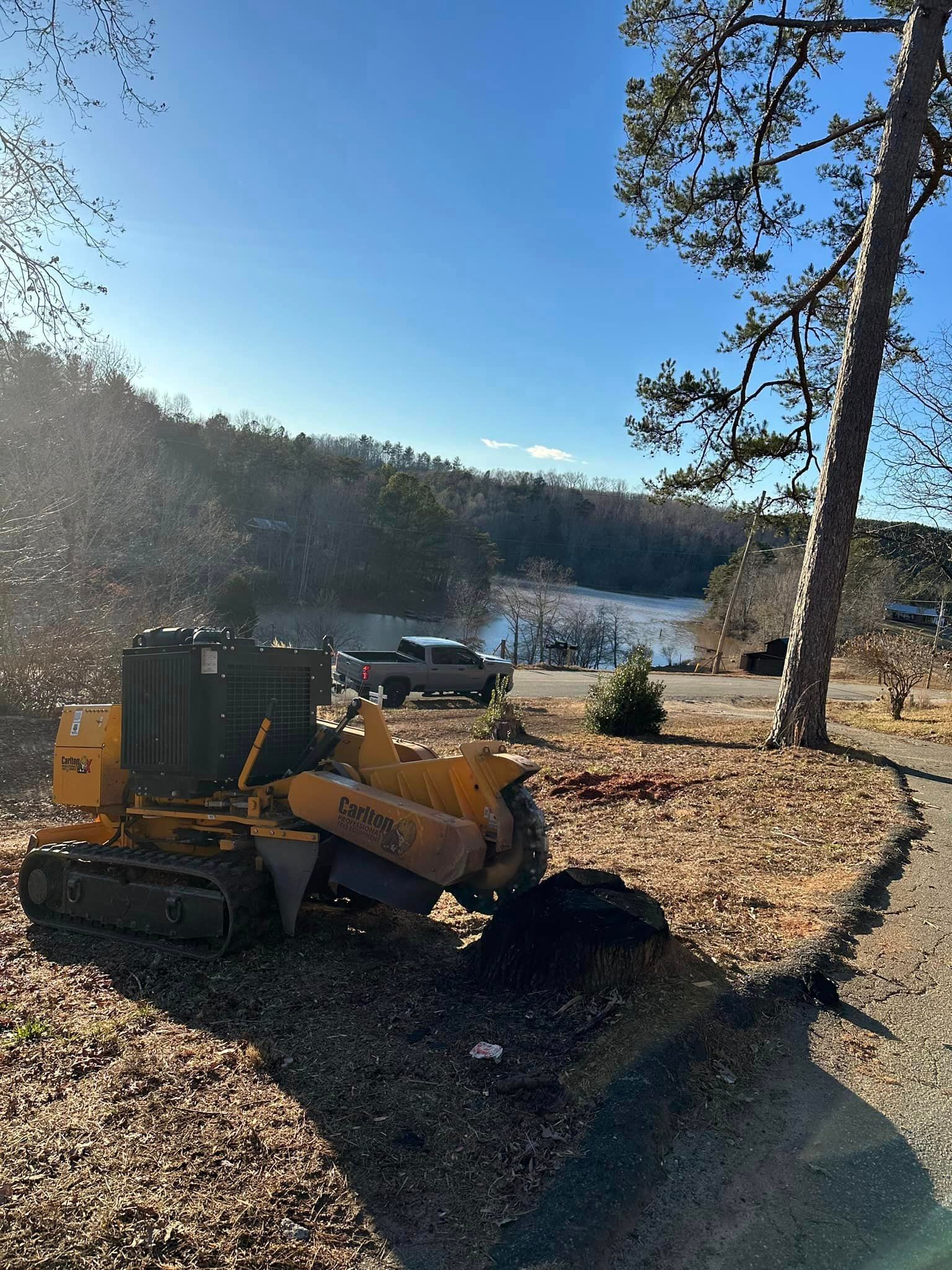 A yellow stump grinder is sitting next to a tree stump.