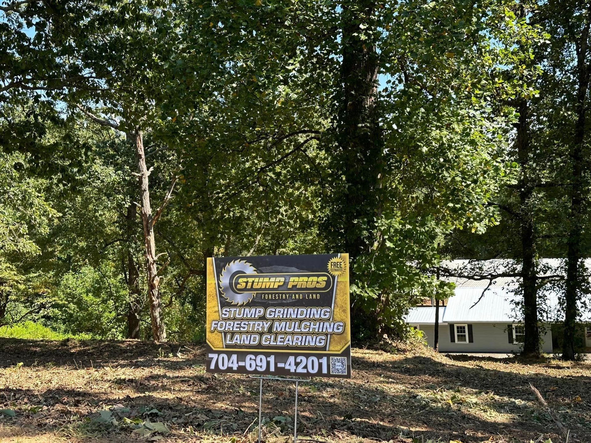 A sign is sitting in the middle of a forest in front of a house.