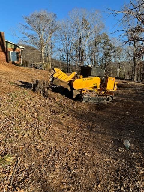 A yellow stump grinder is sitting in a field next to a house.