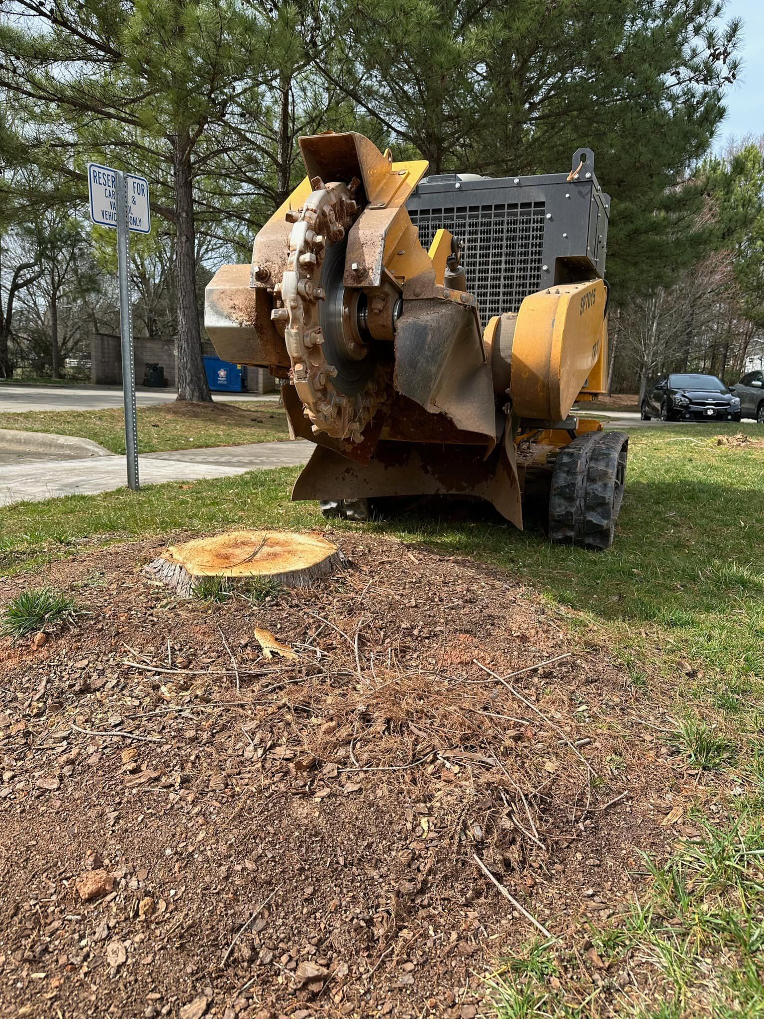A yellow tractor is cutting a tree stump in the grass.