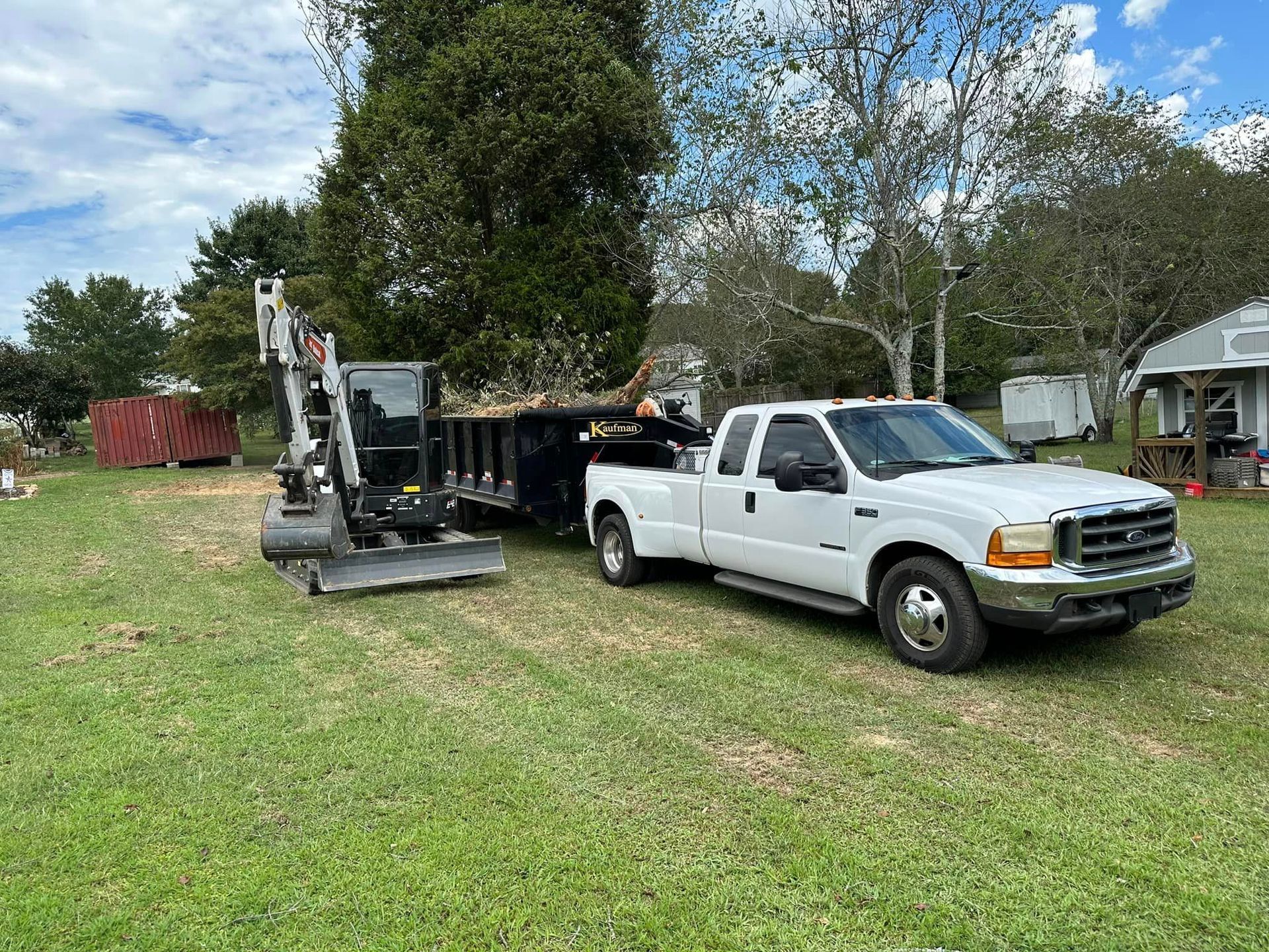 A white truck is towing a dumpster in a grassy field.