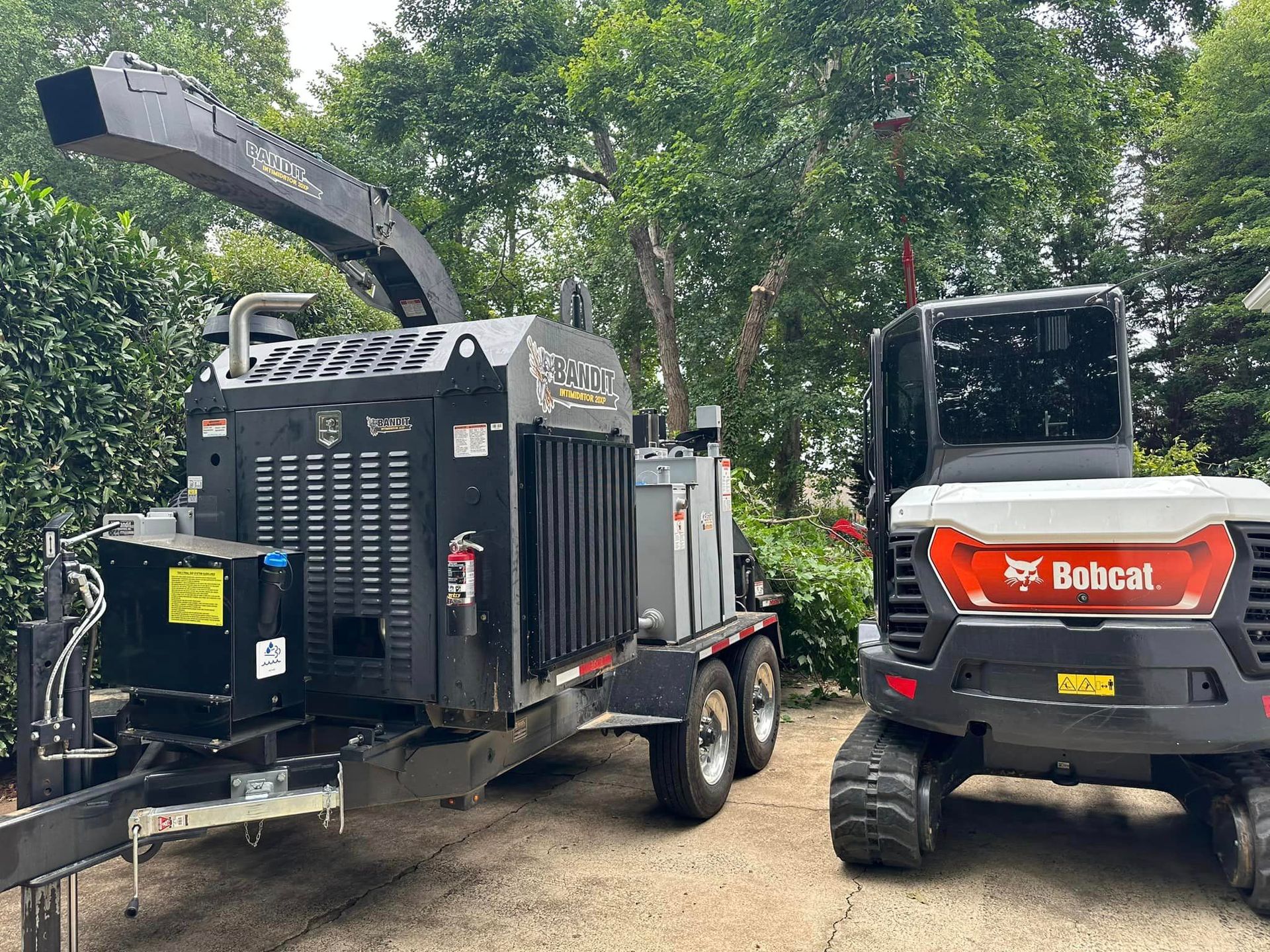 A bobcat chipper and a bobcat excavator are parked next to each other in a driveway.
