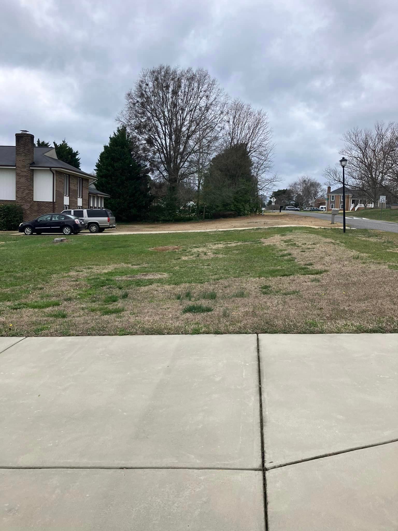 A concrete sidewalk leading to a grassy field with a house in the background.