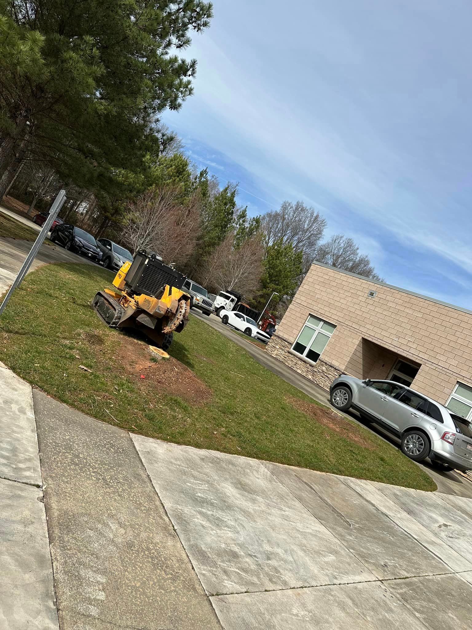A stump grinder is sitting in the grass in front of a building.