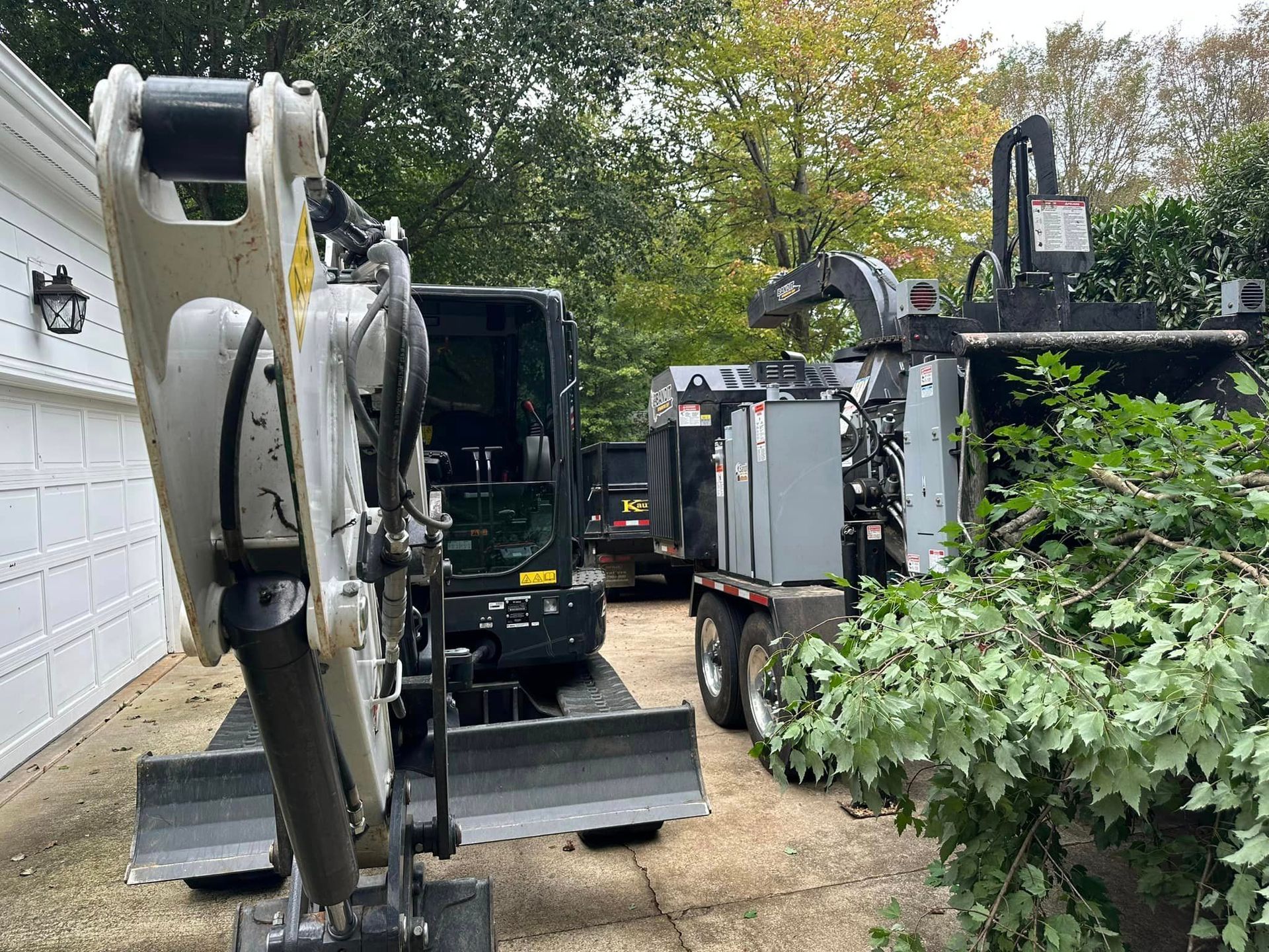 A small excavator is parked in a driveway next to a truck.