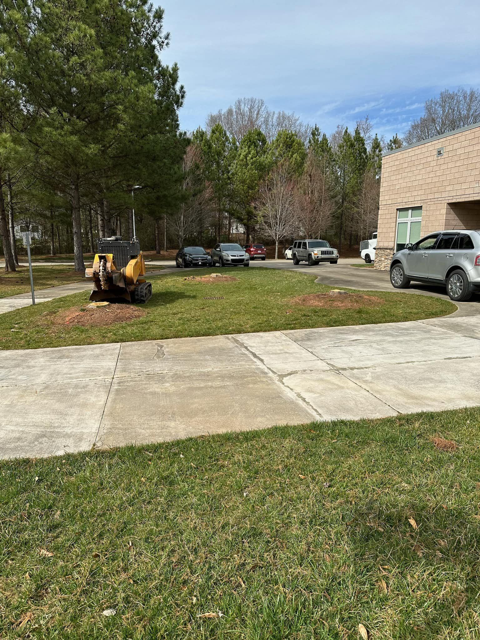 A lawn mower is parked in the grass in front of a building.