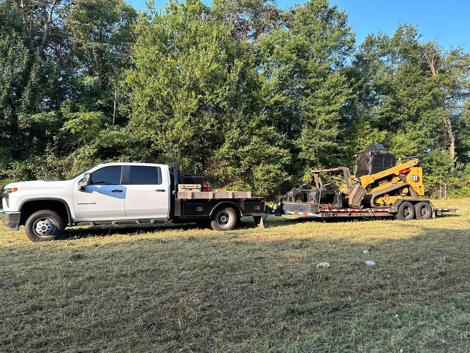 A white truck is towing a yellow tractor on a trailer.
