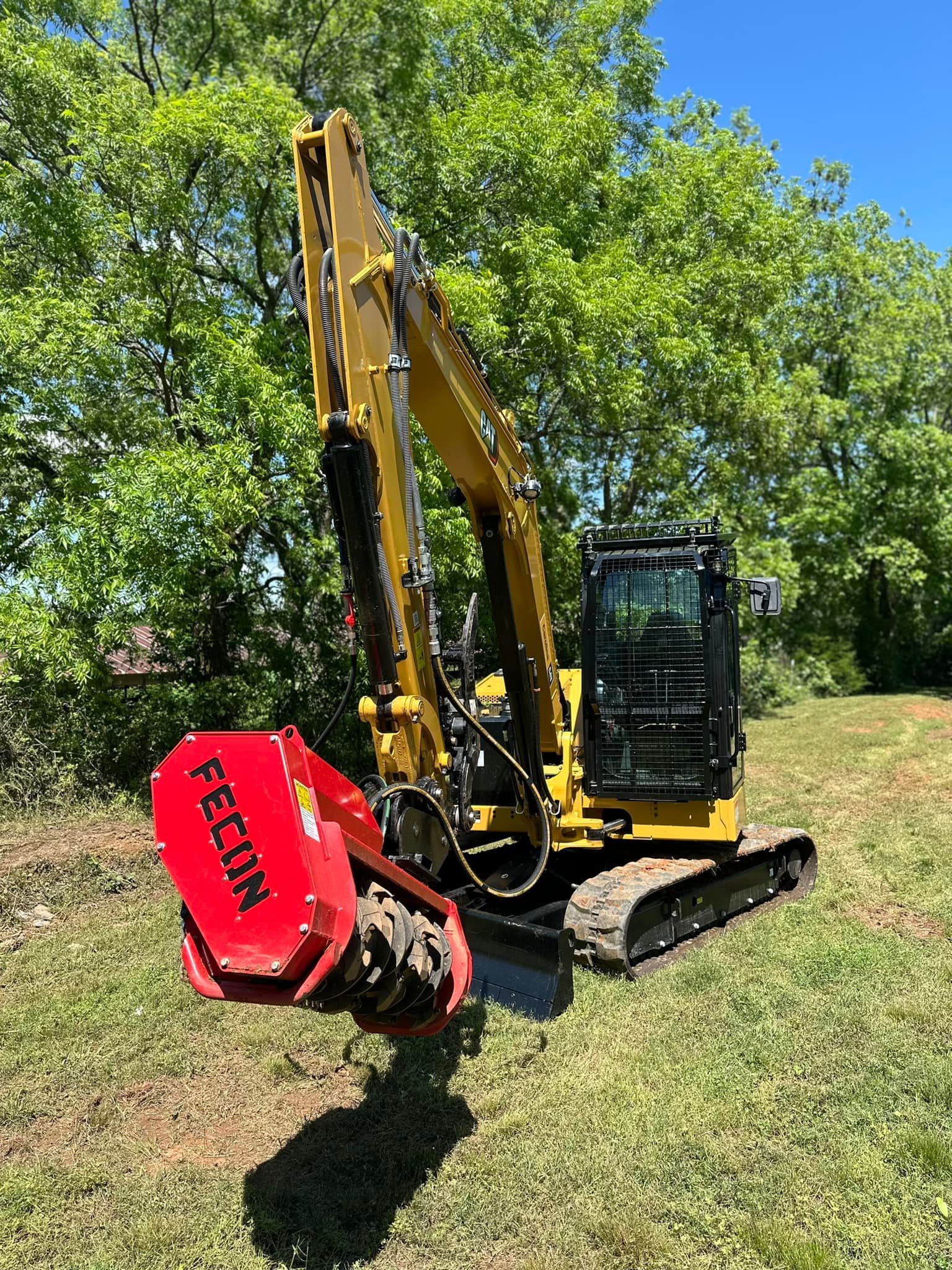 A yellow excavator is parked in a grassy field with trees in the background.
