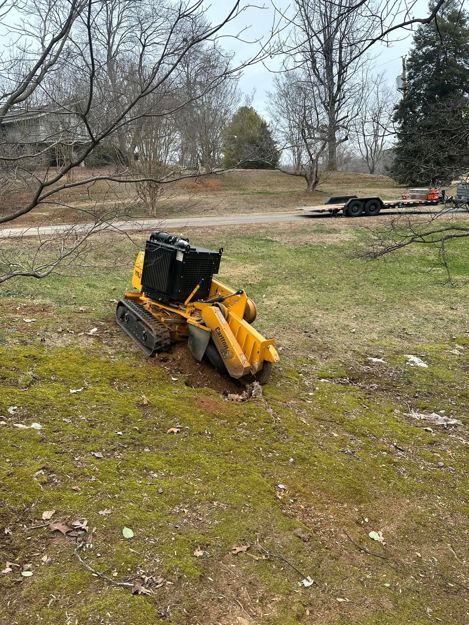 A yellow stump grinder is sitting in the middle of a grassy field.