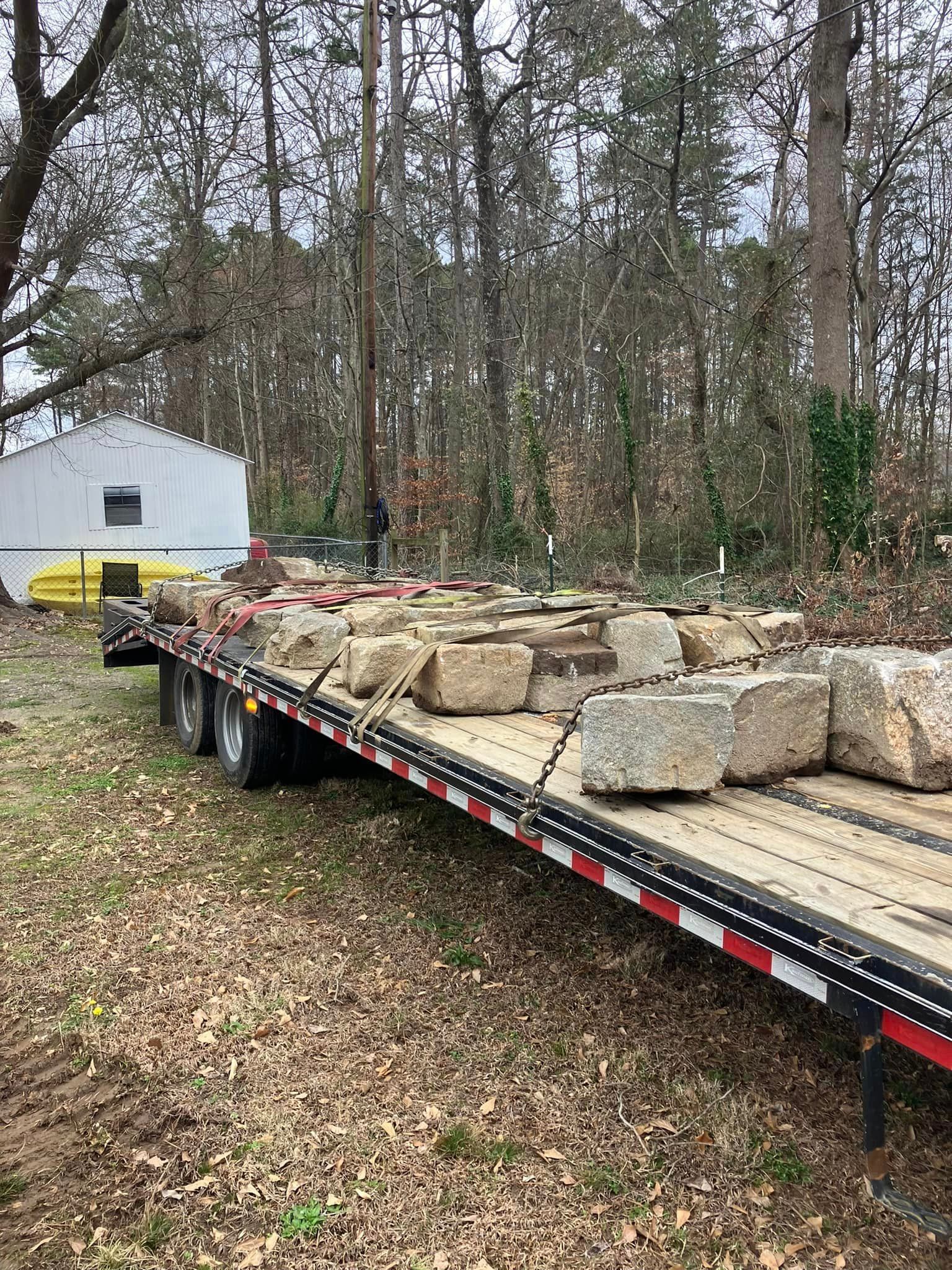 A flatbed trailer filled with rocks is parked in the woods.