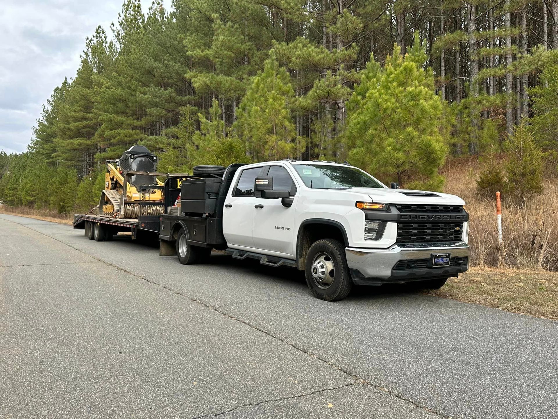A white truck is driving down a road with a trailer attached to it.