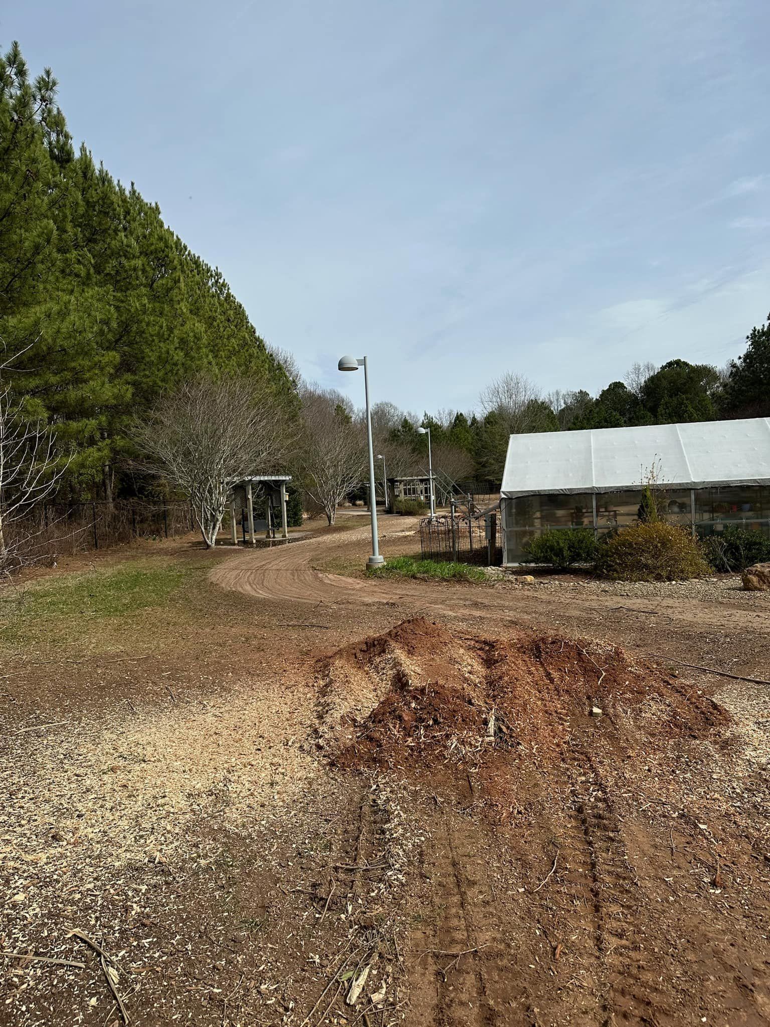 A greenhouse is sitting in the middle of a dirt field surrounded by trees.