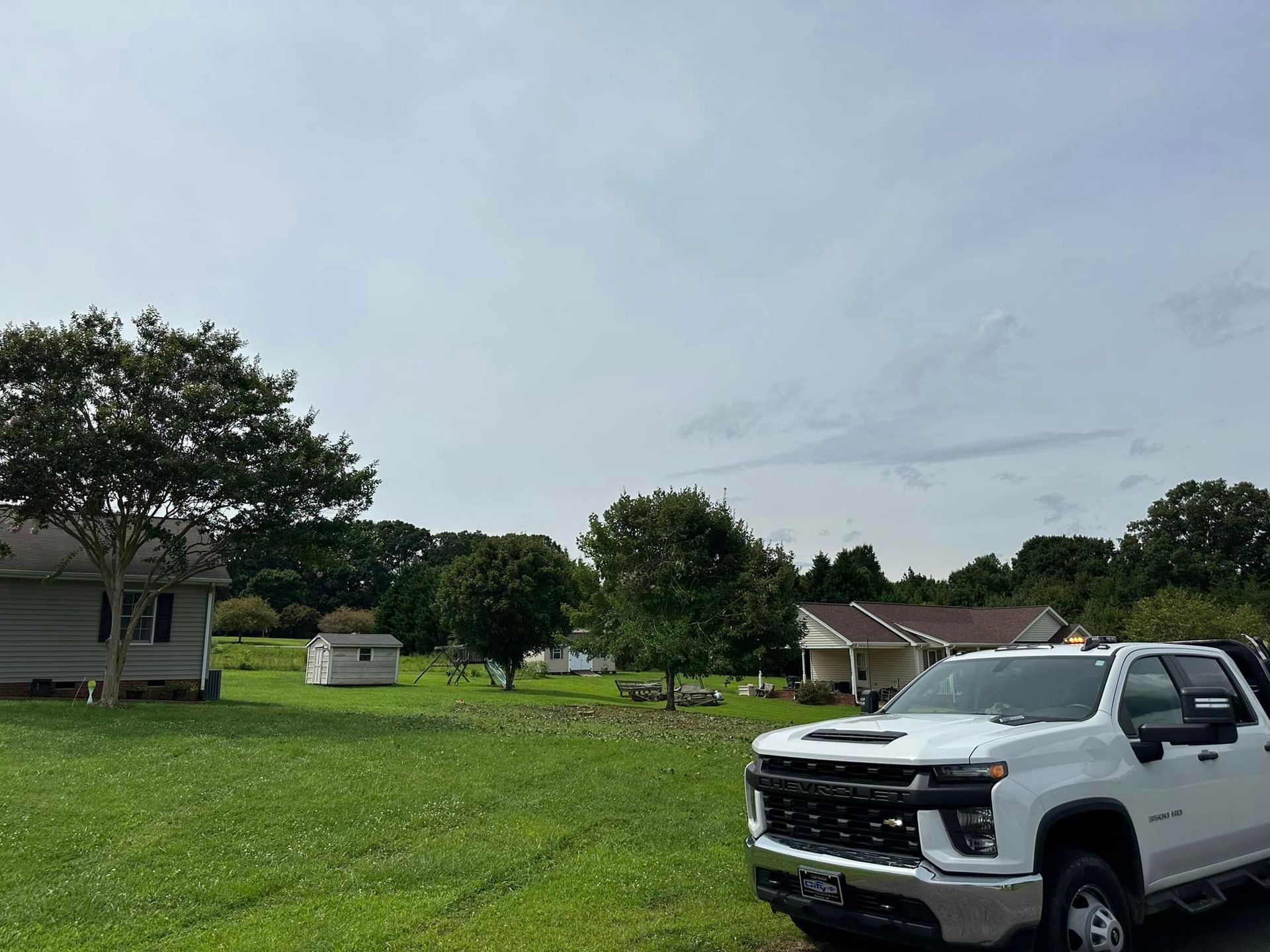 A white truck is parked in a grassy field in front of a house.
