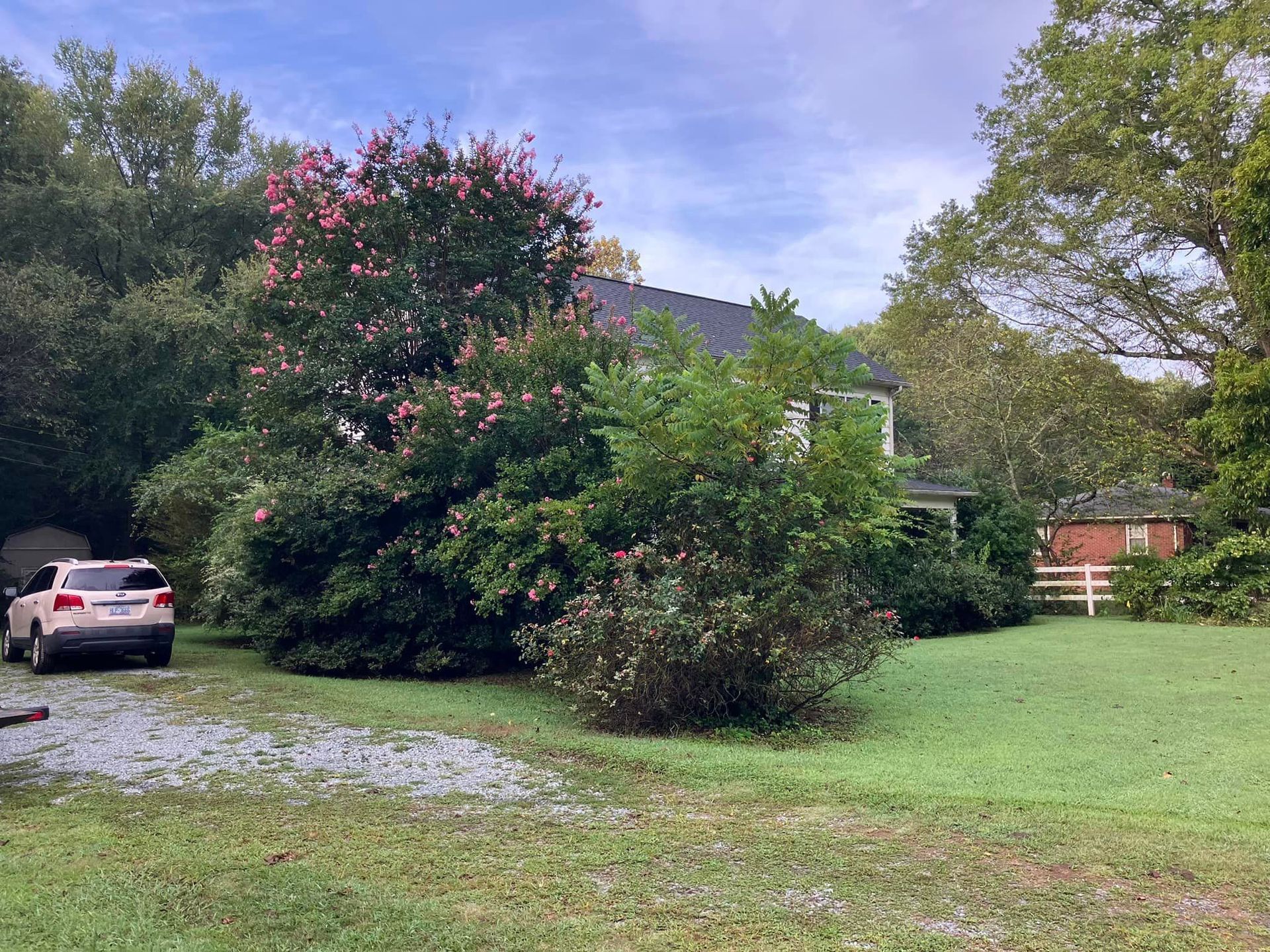 A car is parked in the grass in front of a house.