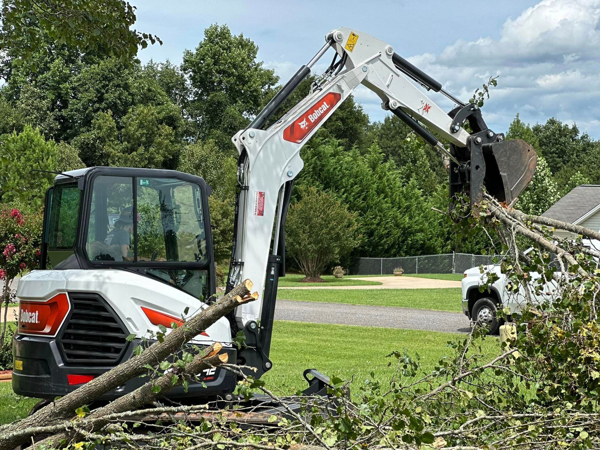 A bobcat excavator is cutting down a tree in a yard.