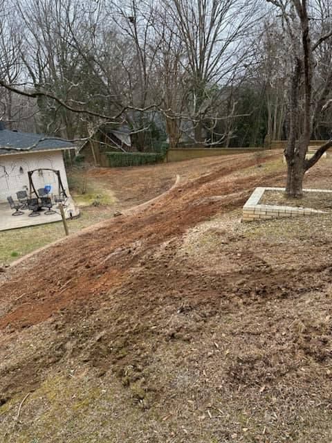 A dirt road going through a backyard with a house in the background.