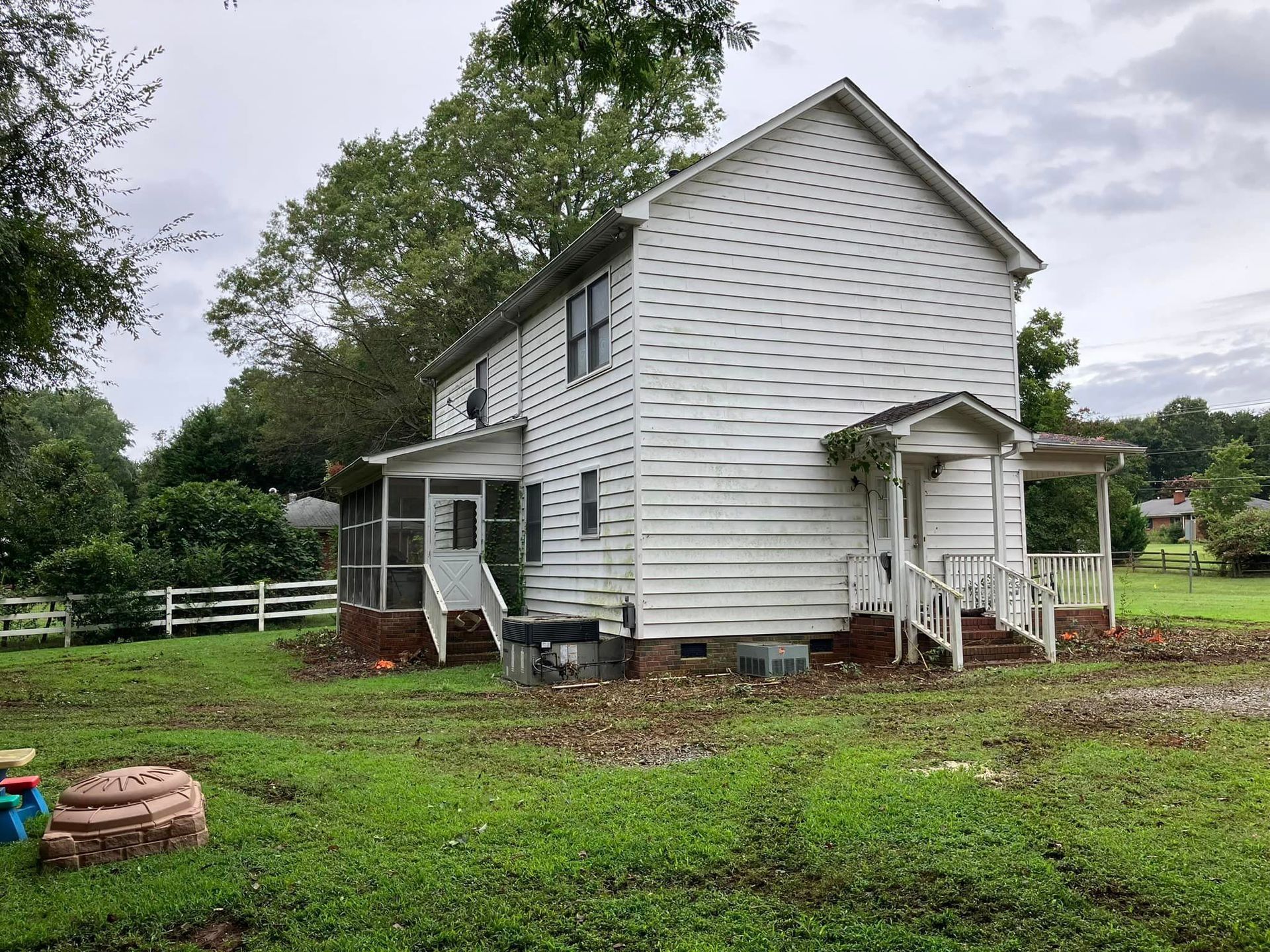 A white house with a porch is sitting in the middle of a grassy field.