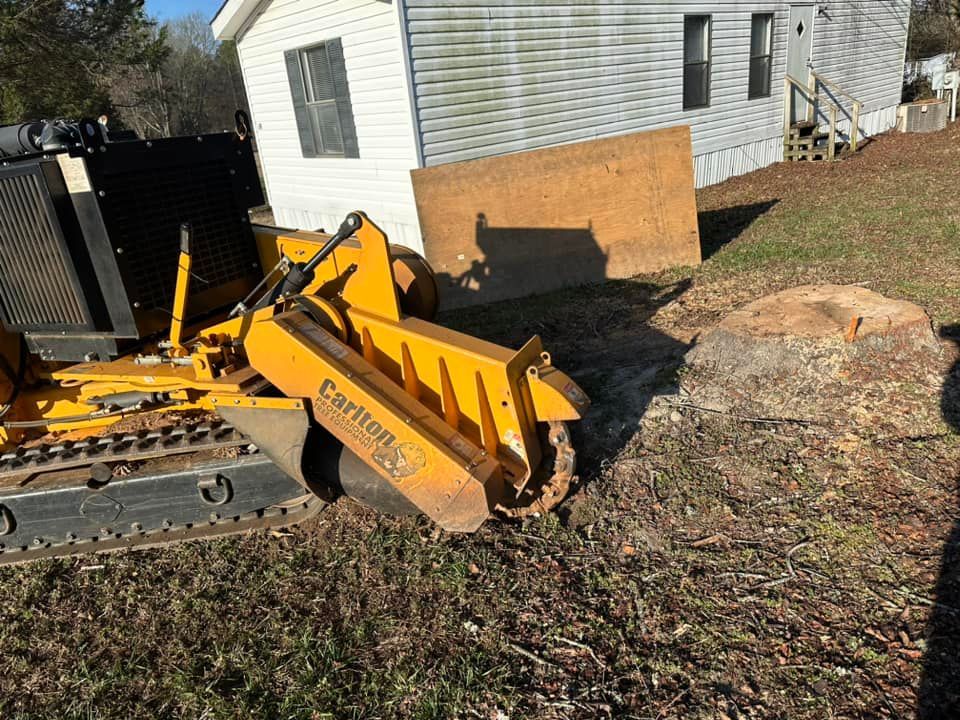 A yellow stump grinder is sitting in front of a house.
