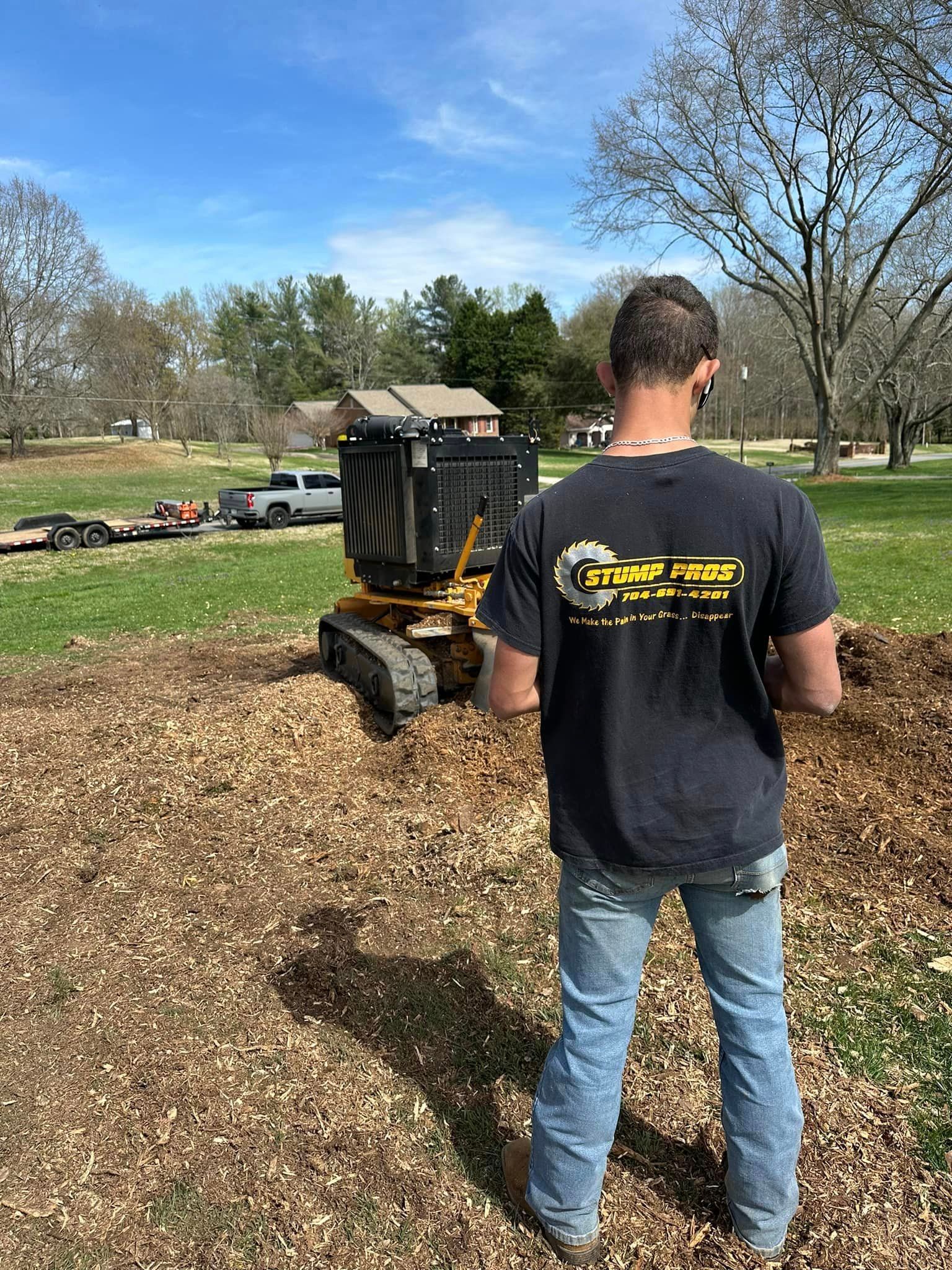 A man is standing in front of a stump grinder in a field.