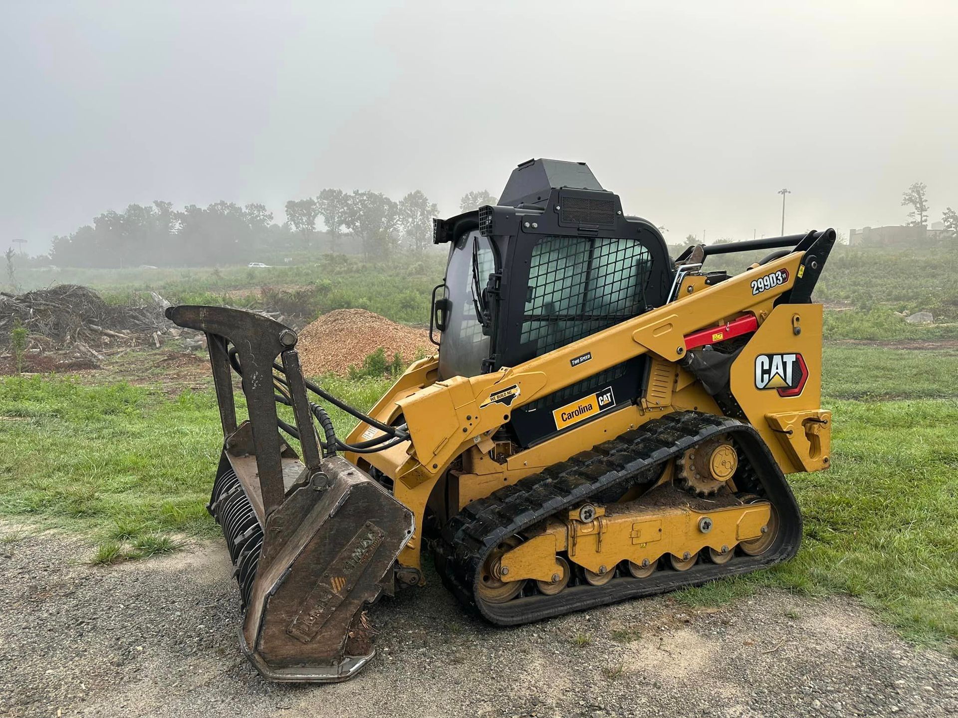 A bulldozer is parked in a grassy field on a foggy day.