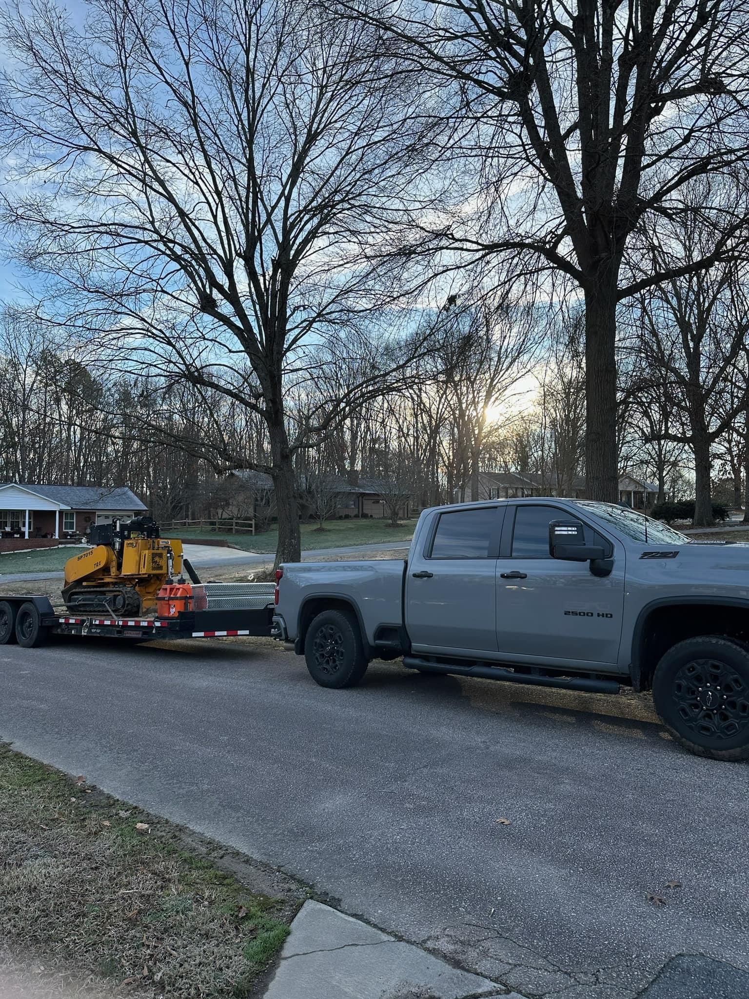 A gray truck is towing a yellow bulldozer on a trailer.