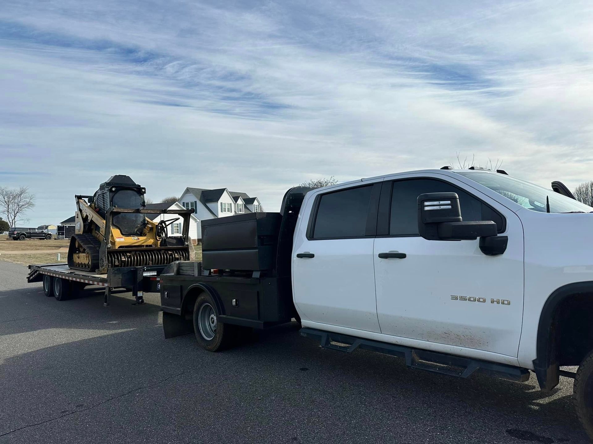 A white truck is towing a bulldozer on a trailer.