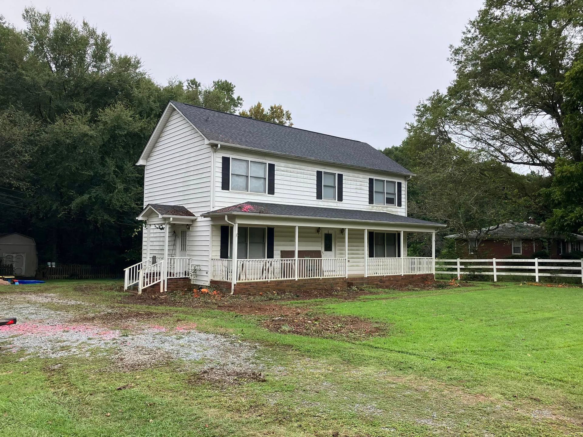 A white house with a porch is sitting in the middle of a grassy field.