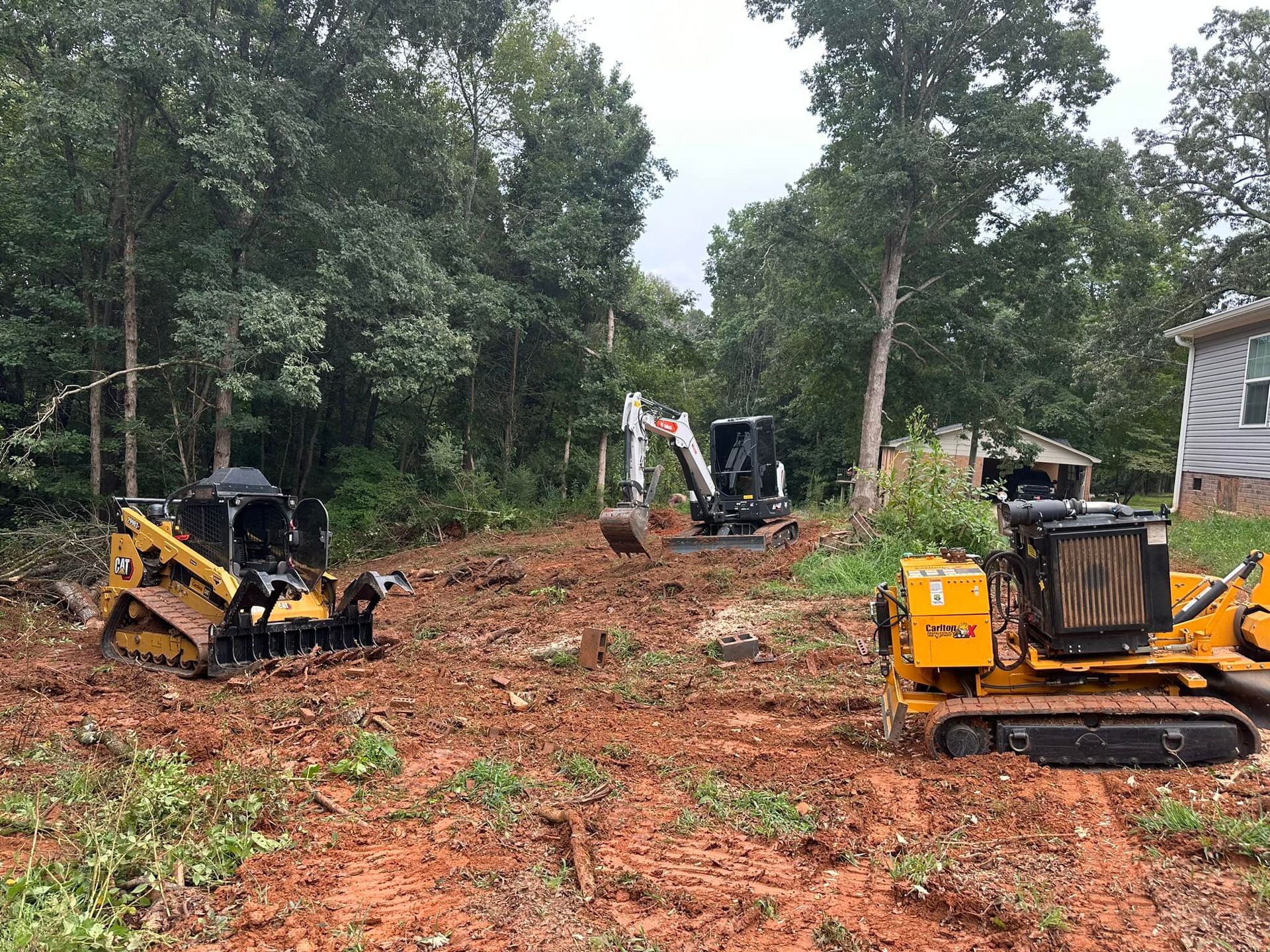Two bulldozers are sitting in a dirt field next to a house.