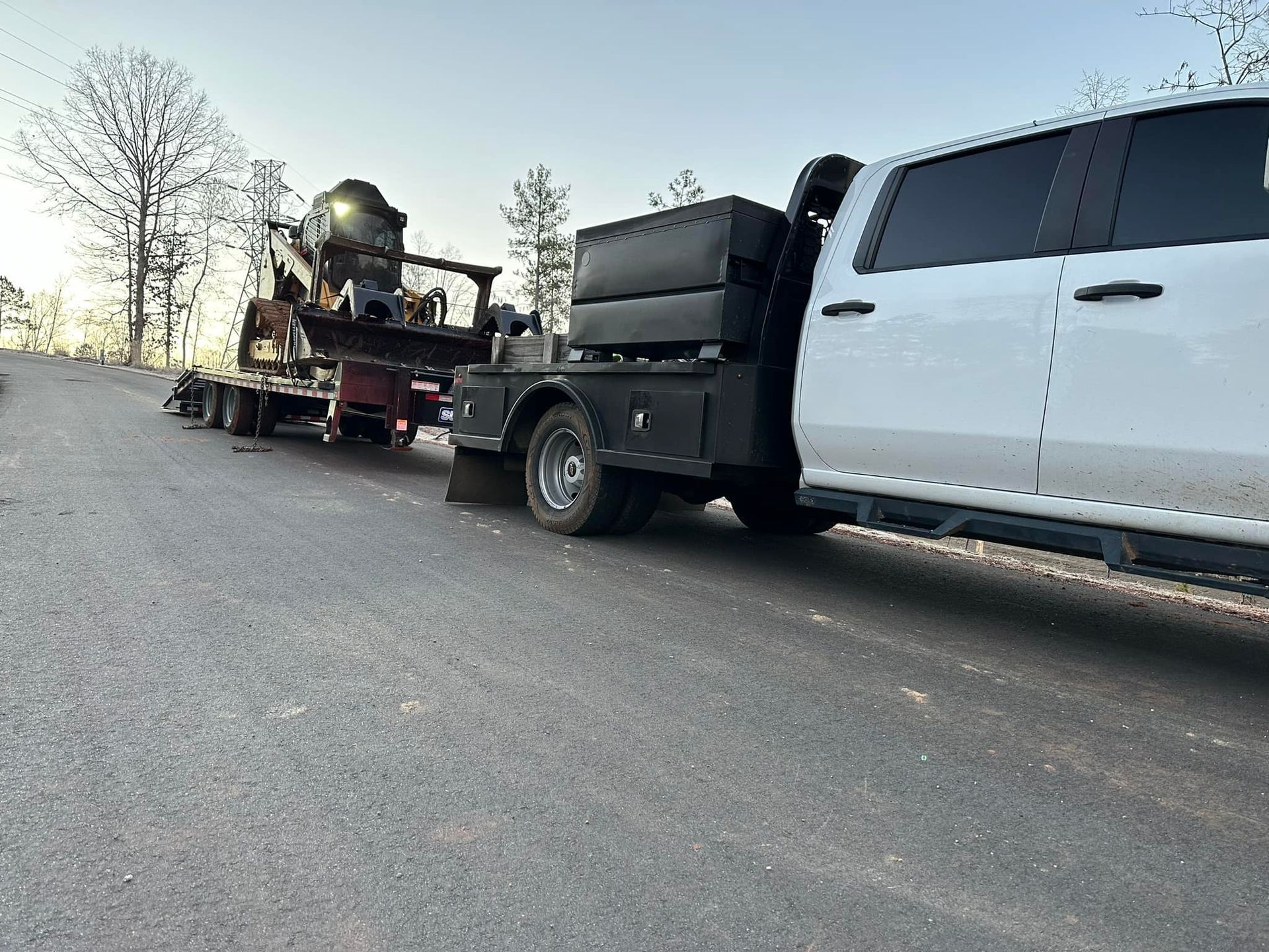 A white truck is towing a trailer on the side of the road.