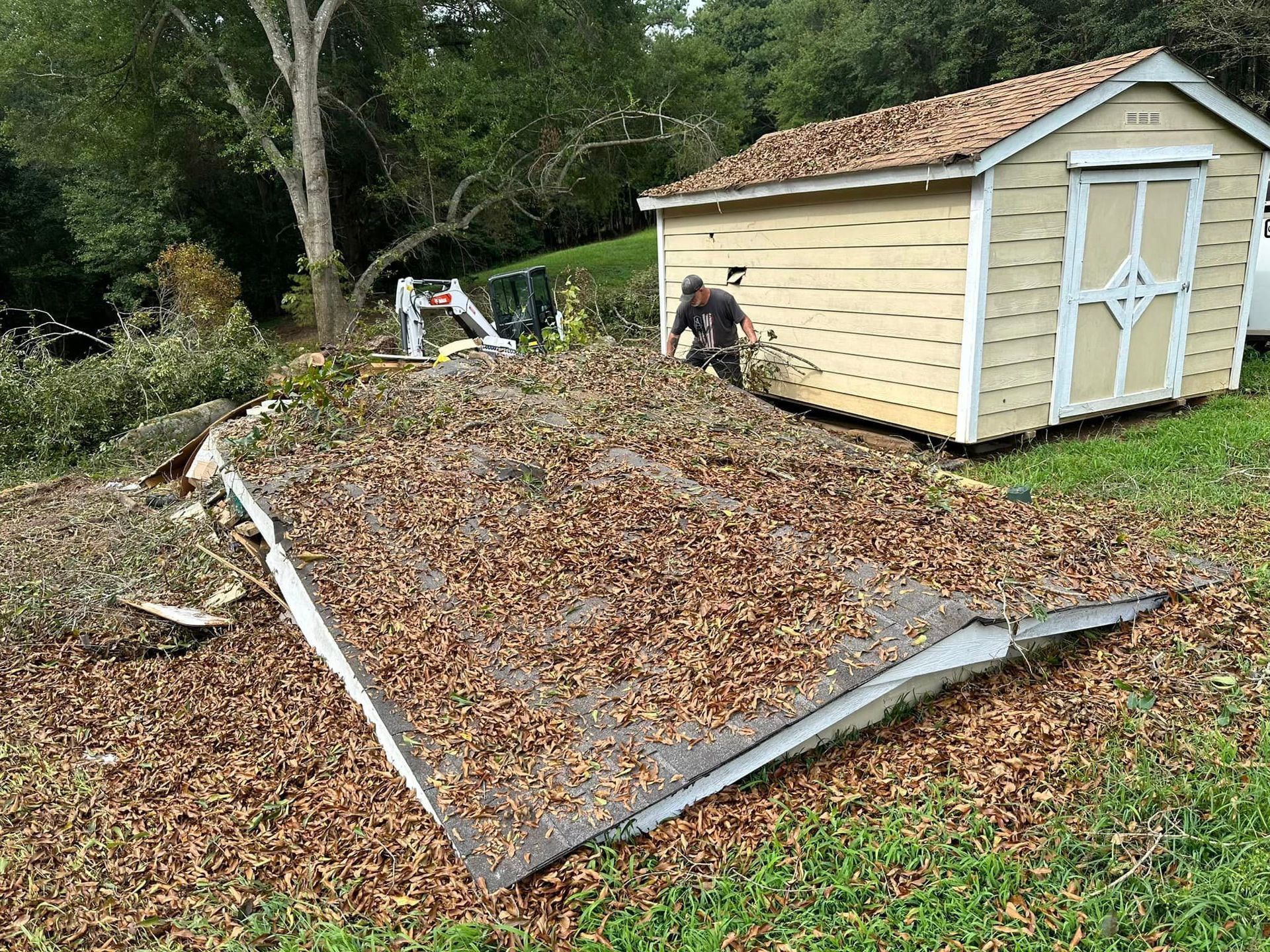 A man is standing on a pile of leaves in front of a shed.