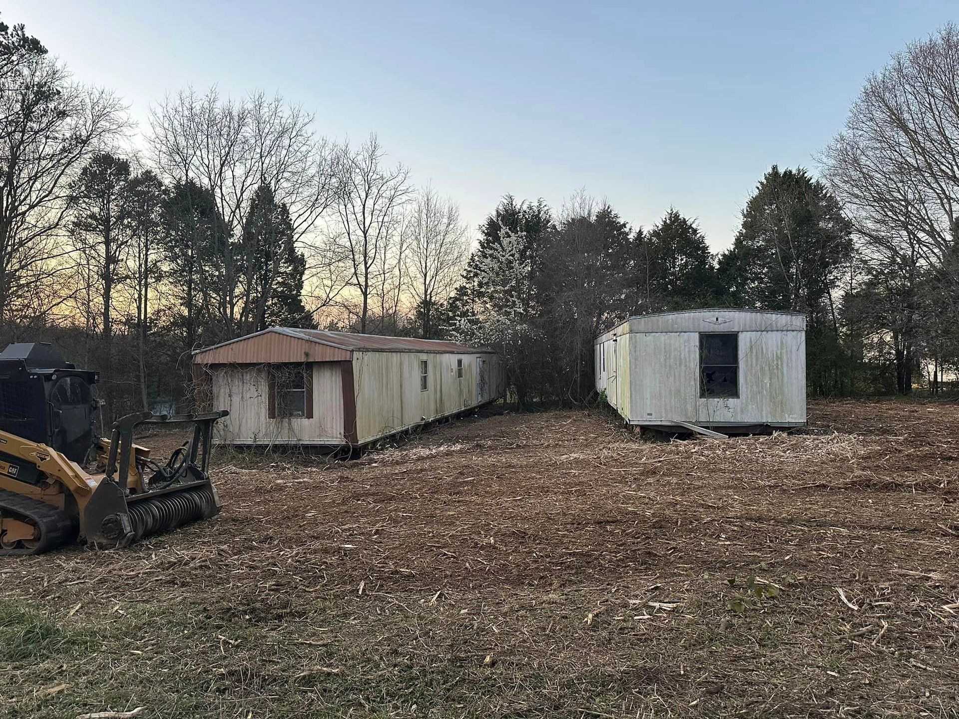 Two mobile homes are sitting in a field next to a bulldozer.