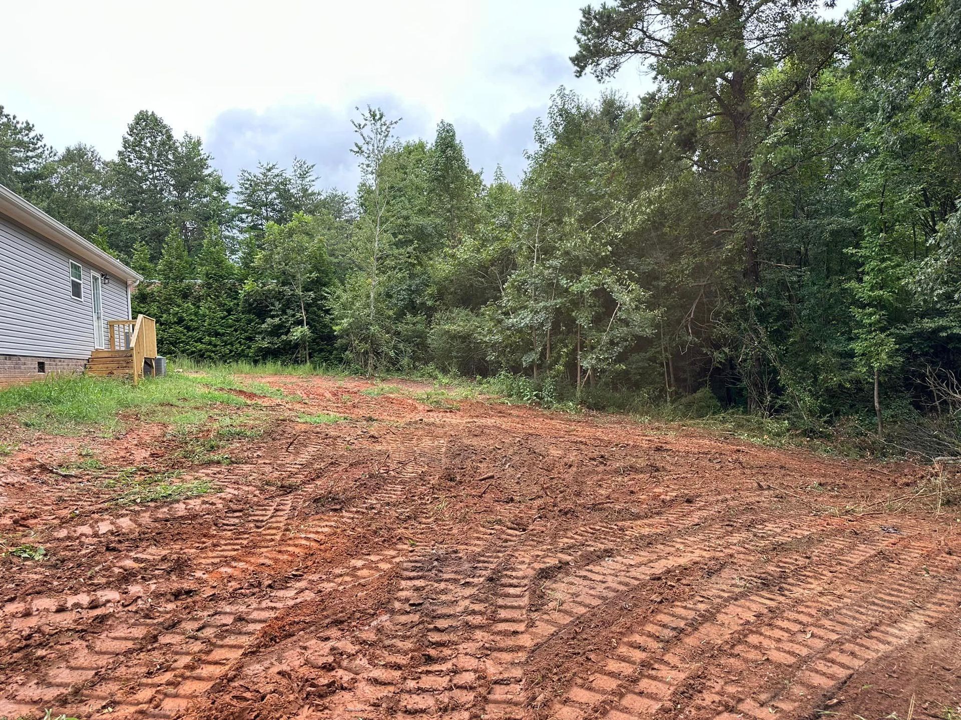 A dirt field with a house in the background and trees in the background.
