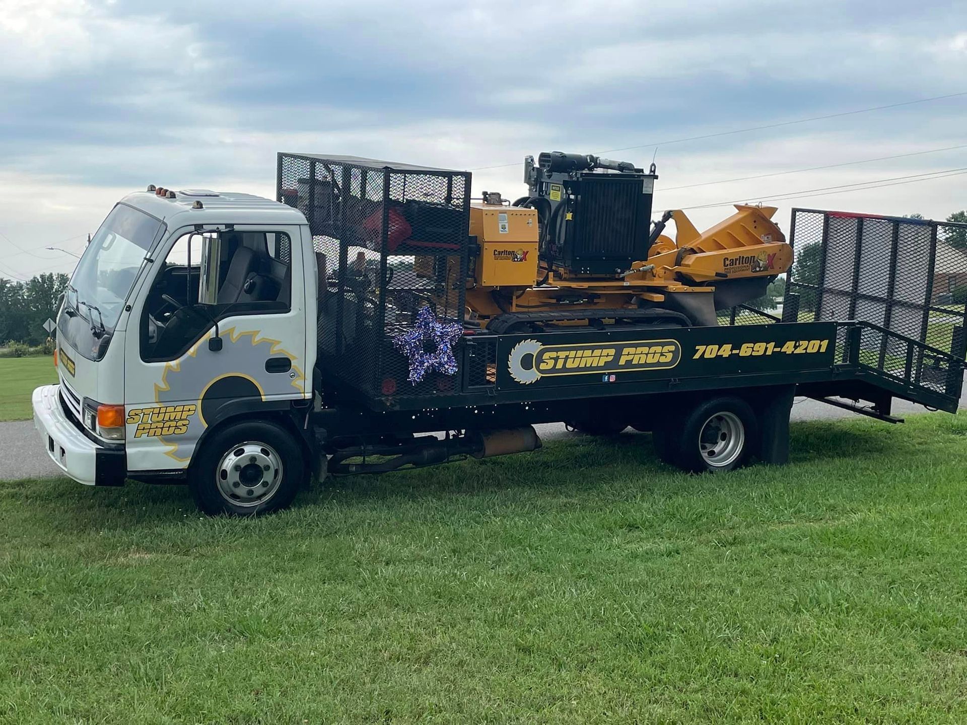 A tow truck with a stump grinder on the back is parked in a grassy field.
