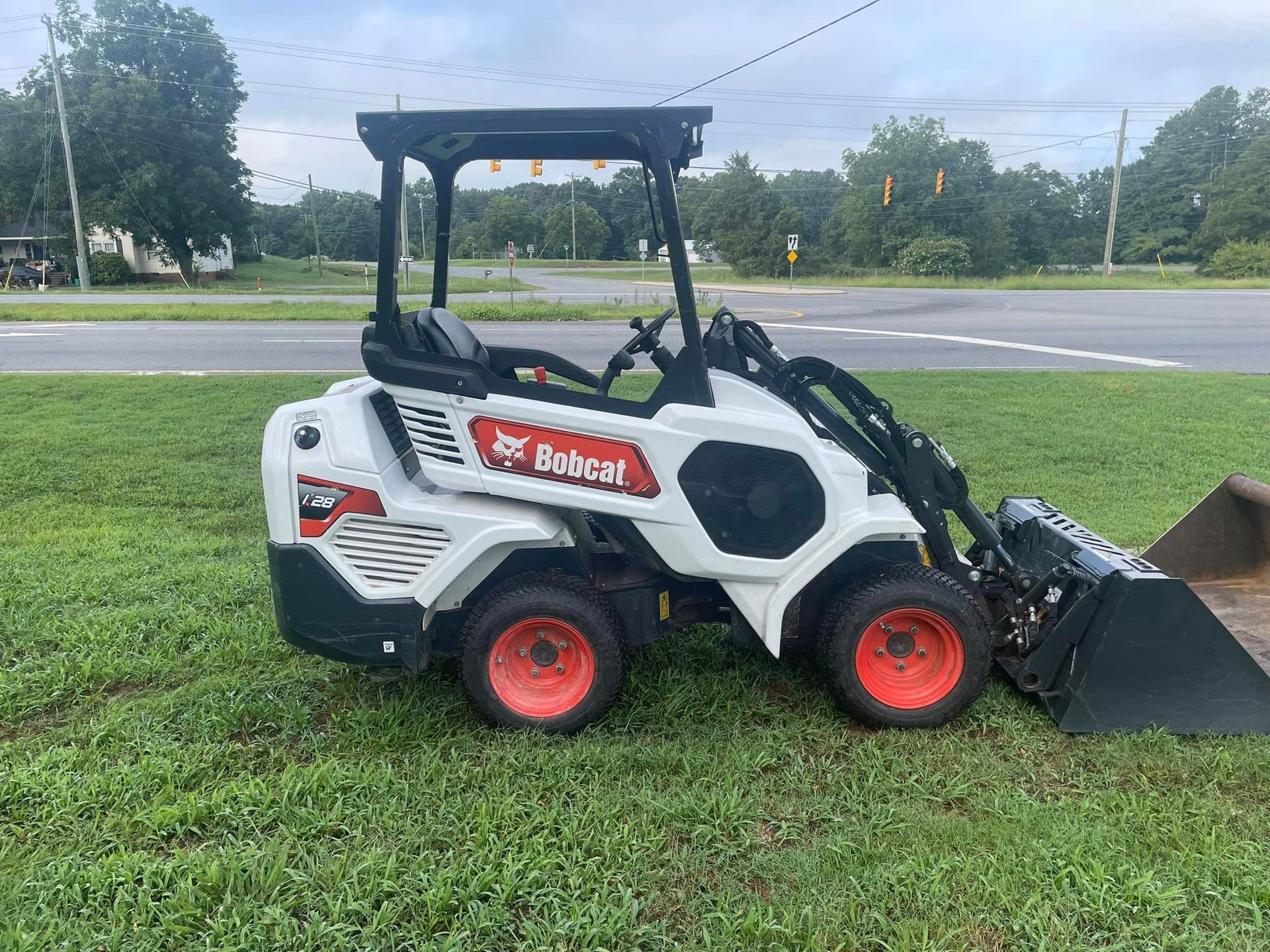 A bobcat loader is parked in the grass next to a road.