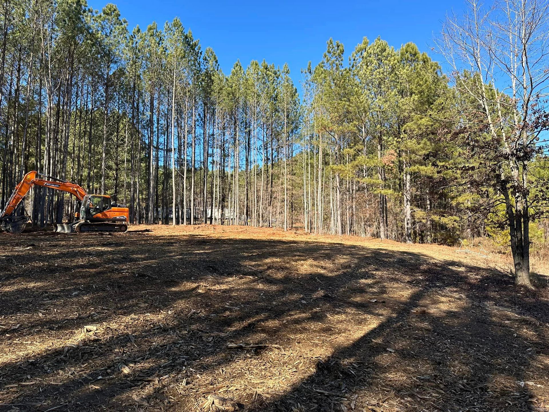 An excavator is working in a field surrounded by trees.