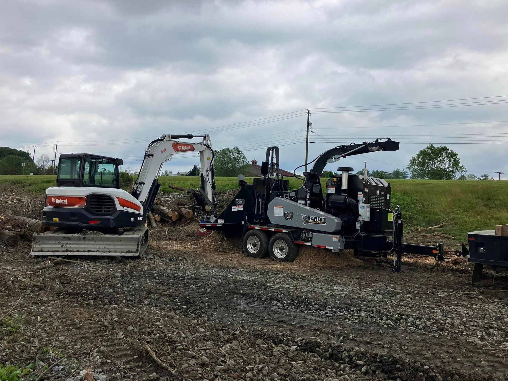 A bulldozer and a wood chipper are parked in a dirt field.