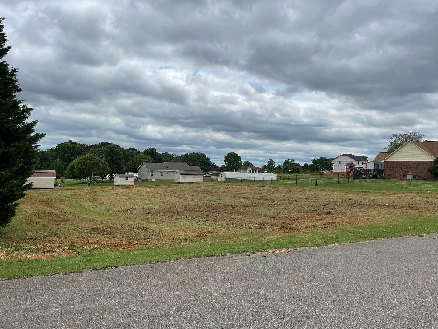 A large grassy field with houses in the background and a cloudy sky.