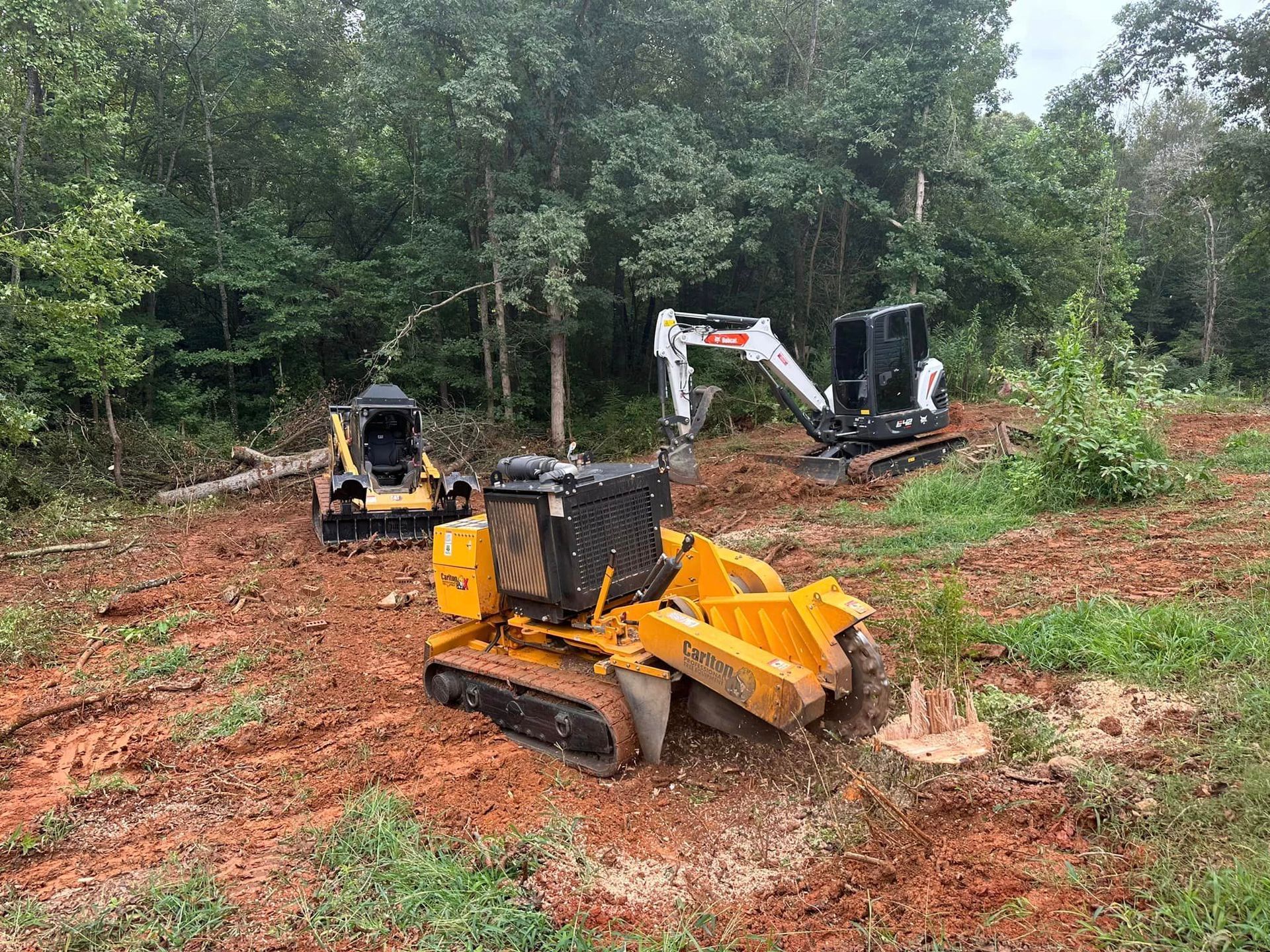A bulldozer and a stump grinder are working in a field.