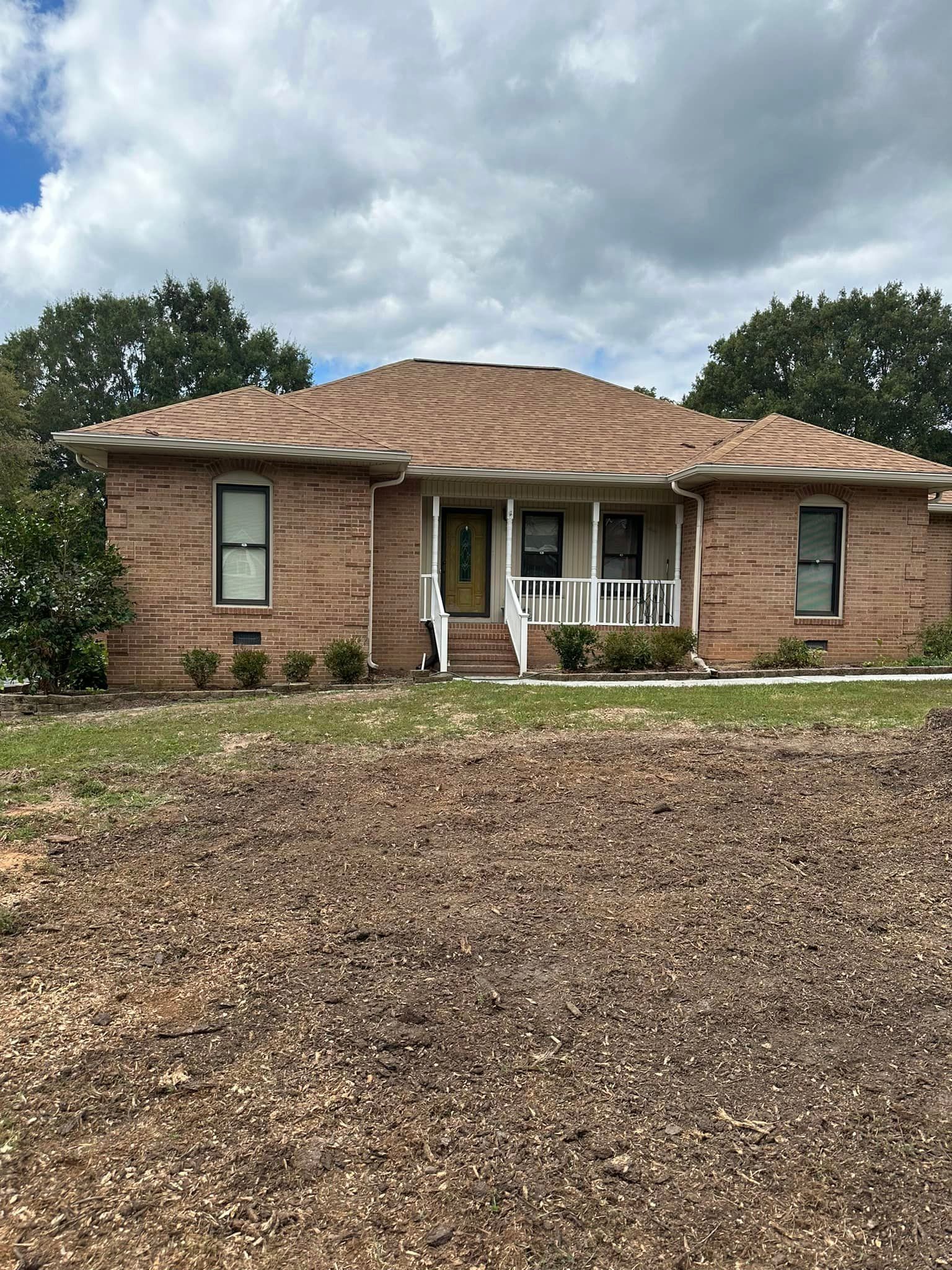 A brick house with a porch and a lot of dirt in front of it.