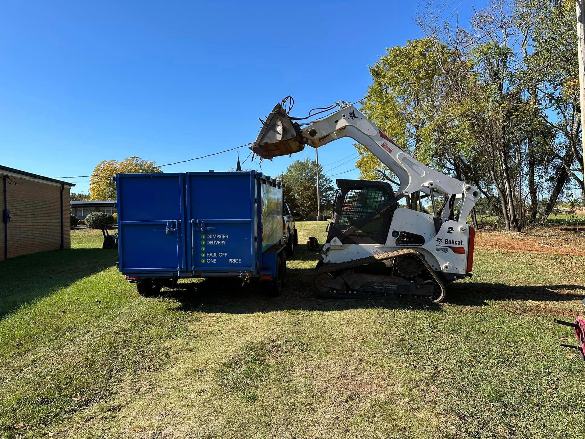 A bulldozer is loading dirt into a blue dumpster.