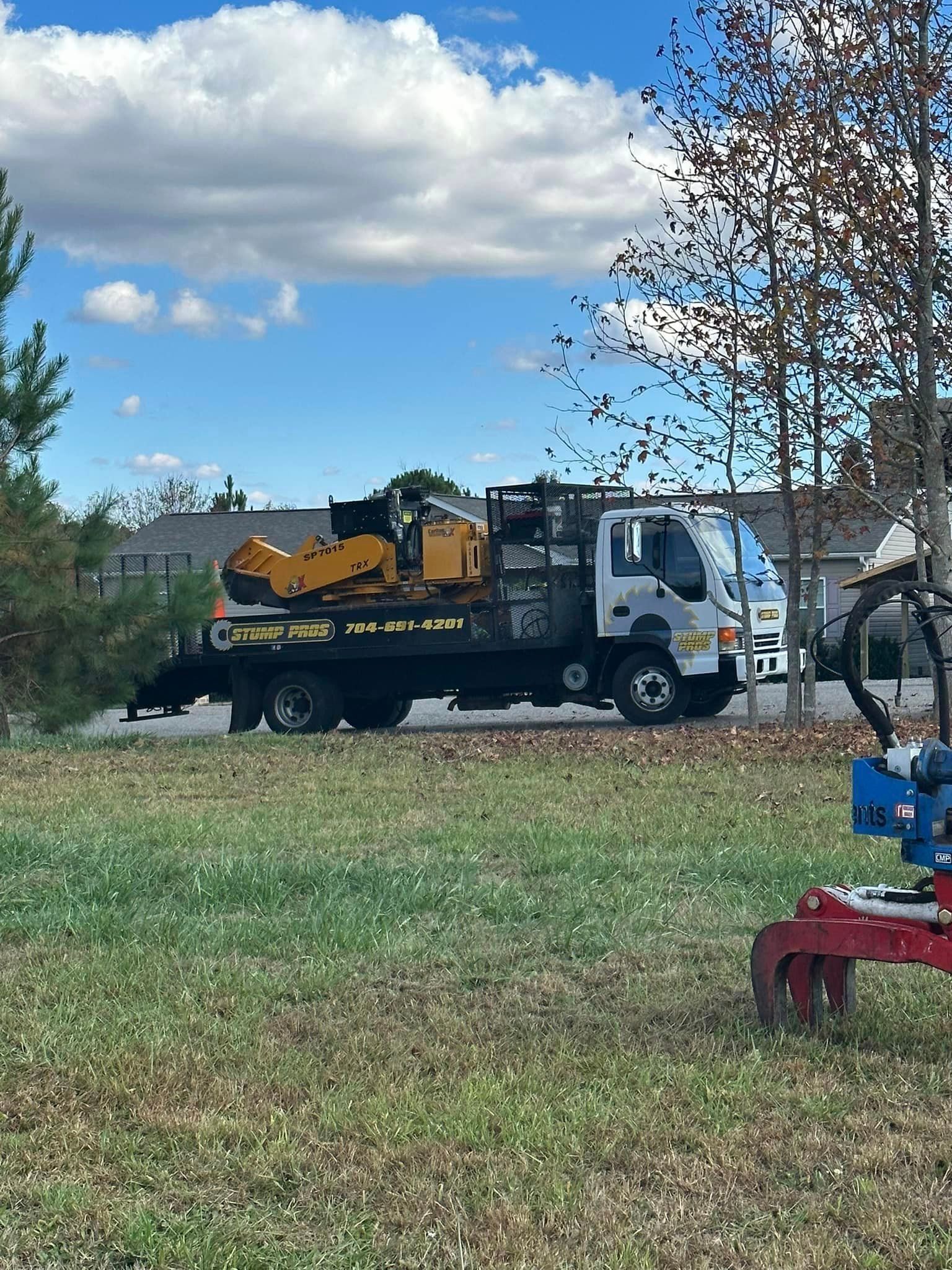 A tow truck is carrying a stump grinder on the back of it.