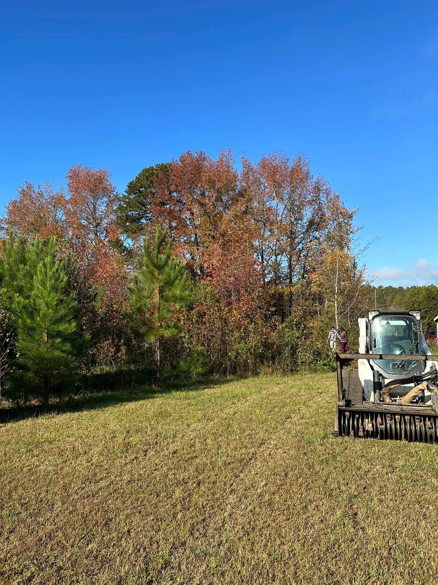 A tractor is plowing a field with trees in the background on a sunny day.