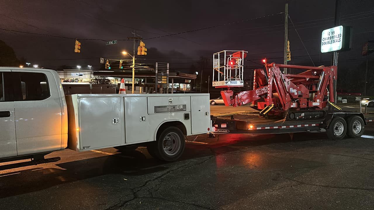 A white truck is towing a red crane on a trailer.