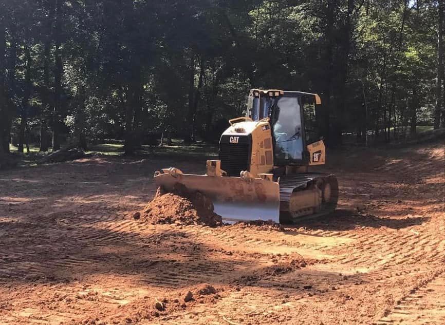 A bulldozer is moving dirt in a field with trees in the background